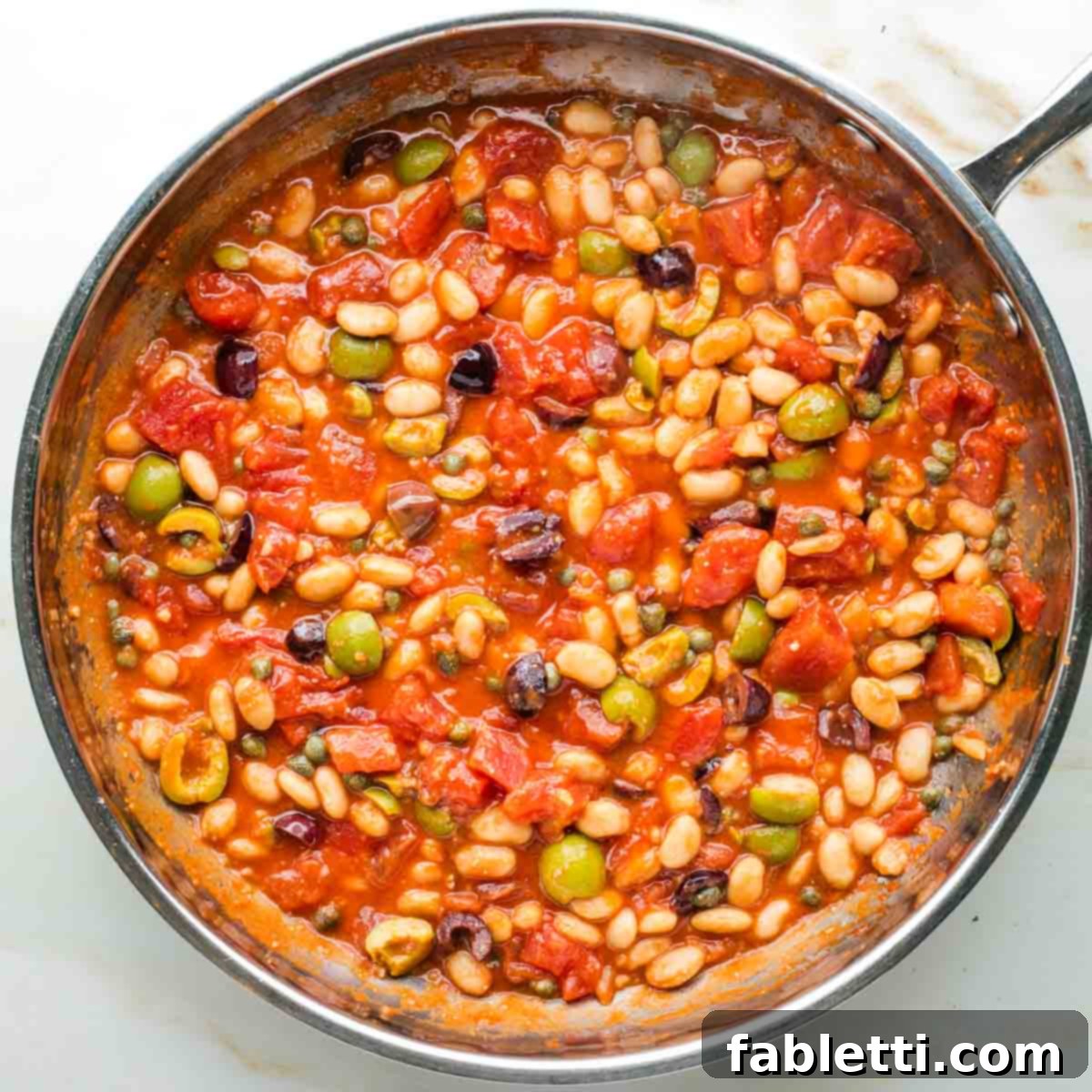 Zesty White Bean Puttanesca Pasta 8 Puttanesca sauce simmering in a skillet with tomatoes, olives, capers, and white beans.