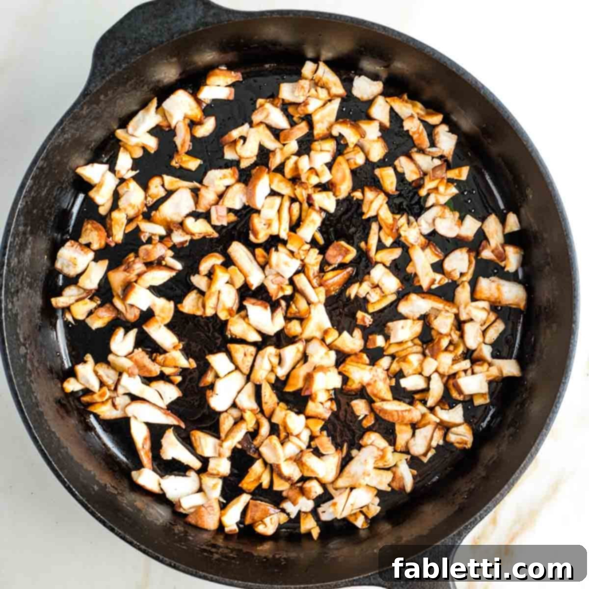 Smoky Shiitake and Zesty Russian Vegan Wedge 11 Diced shiitake mushrooms cooking in oil and tamari in a cast iron skillet, starting to brown and crisp.