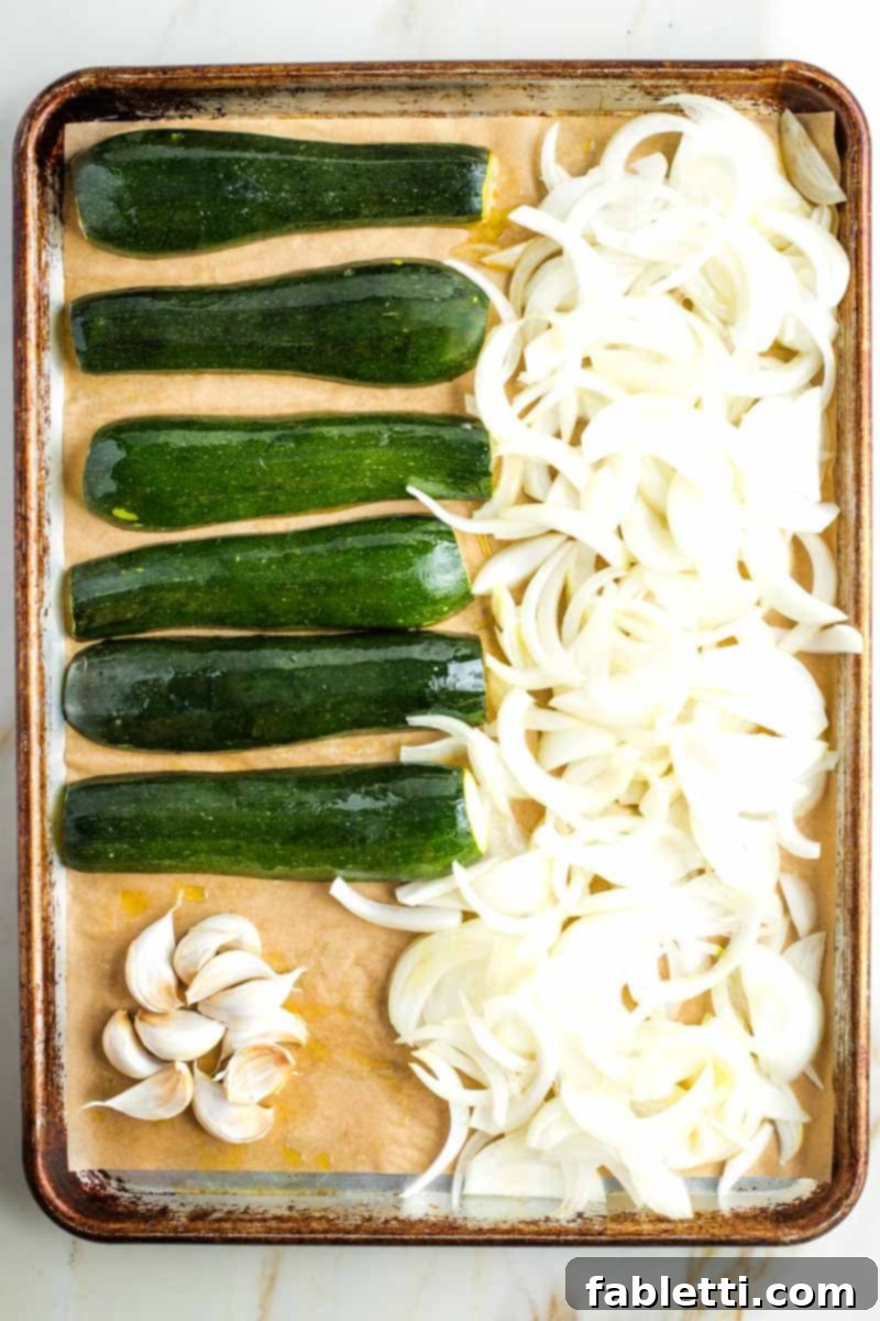 Caramelized Zucchini and Onion Creamy Dip 7 Close-up of zucchini, onions, and garlic on a parchment-lined baking tray, thoroughly coated with olive oil and arranged for roasting.