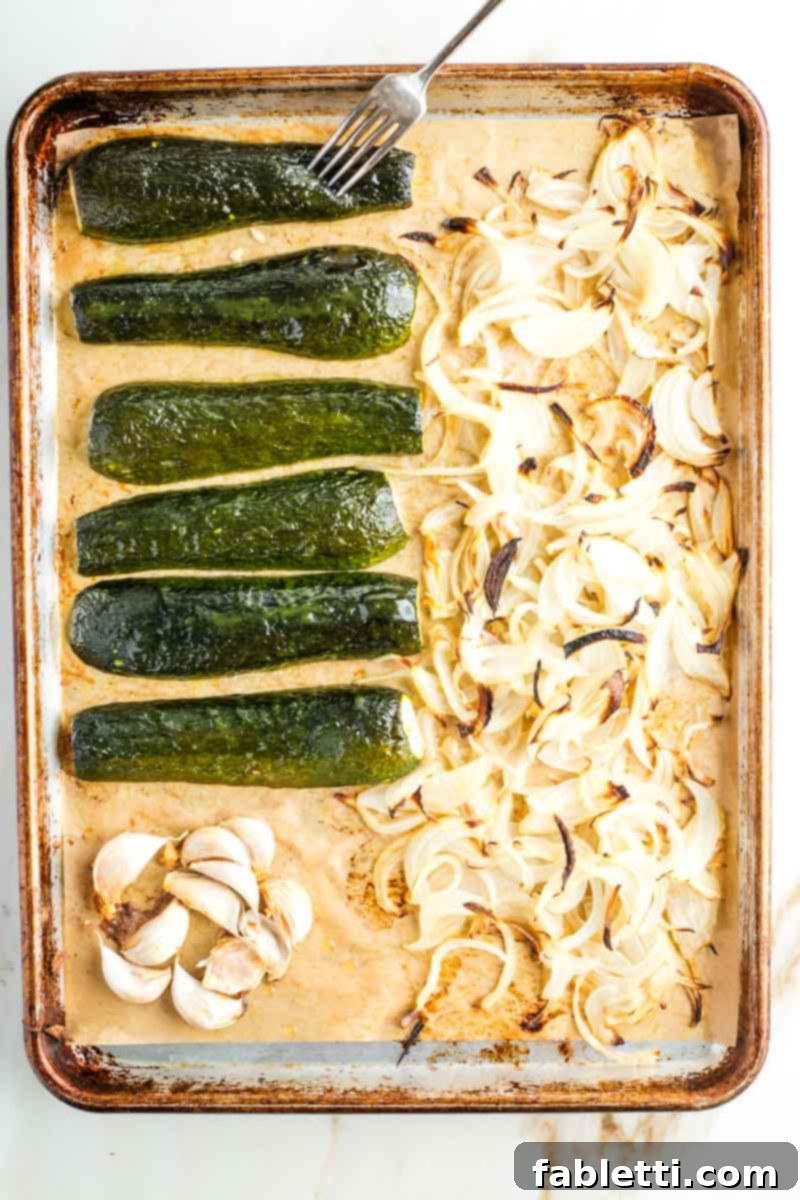 Caramelized Zucchini and Onion Creamy Dip 8 A baking tray showcasing perfectly roasted halved zucchini, caramelized sliced onions, and soft garlic cloves on parchment paper, fresh out of the oven.
