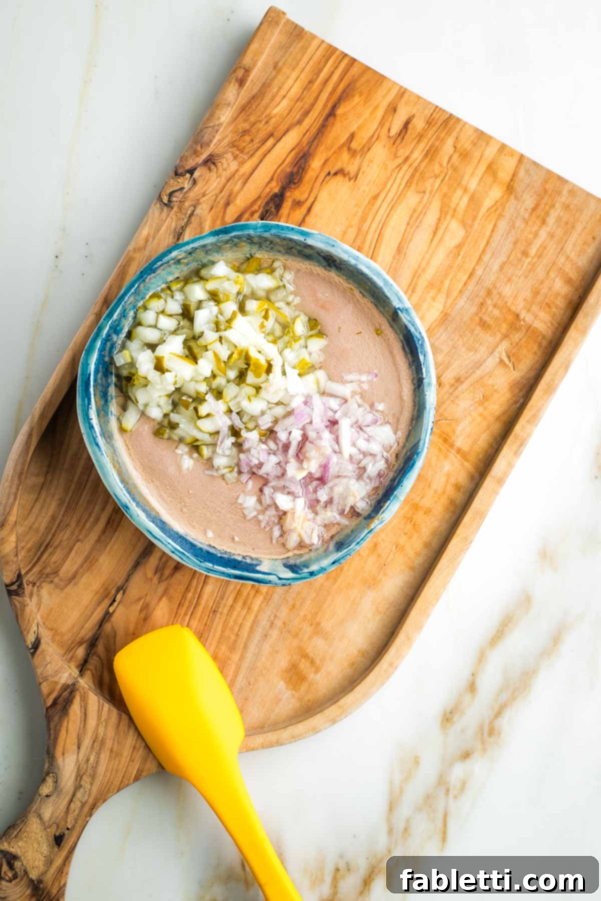 Diced pickles and minced shallot on top of a creamy orange dressing in a small bowl. 