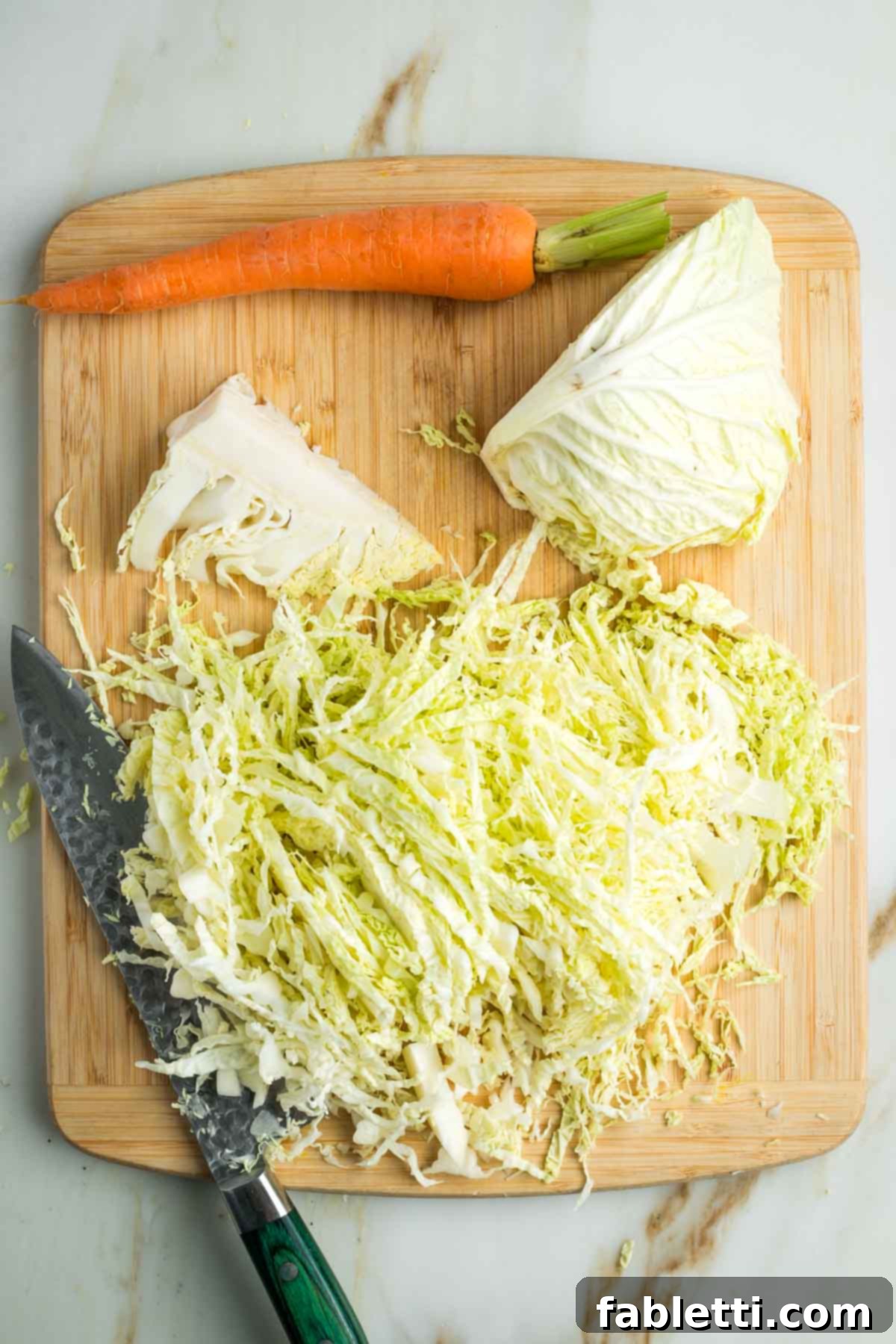 Thinly slicing cabbage from a half head on a cutting board.