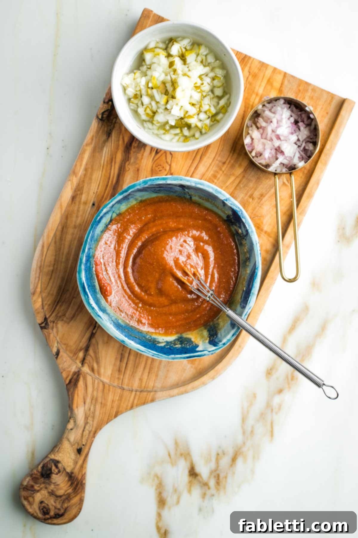 Whisking tomato paste into a tahini and tamari situation with diced pickles and shallot in small bowls off to the side.