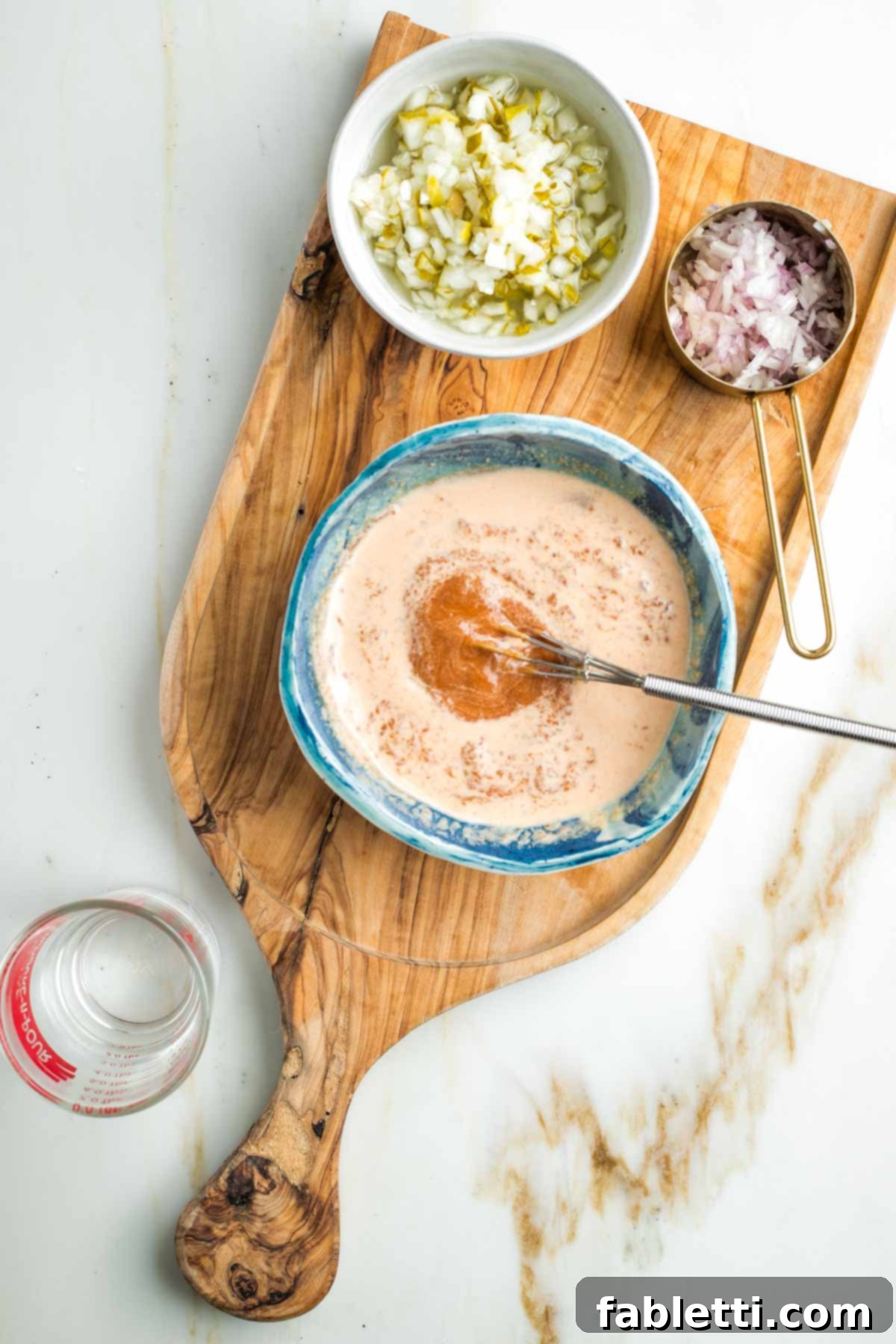 Whisking water into a pasty red sauce in a small bowl.