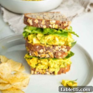Zingy Vegan Tofu Egg Salad 19 Tofu egg salad on sourdough, stacked with green lettuce in between and chips on the side.