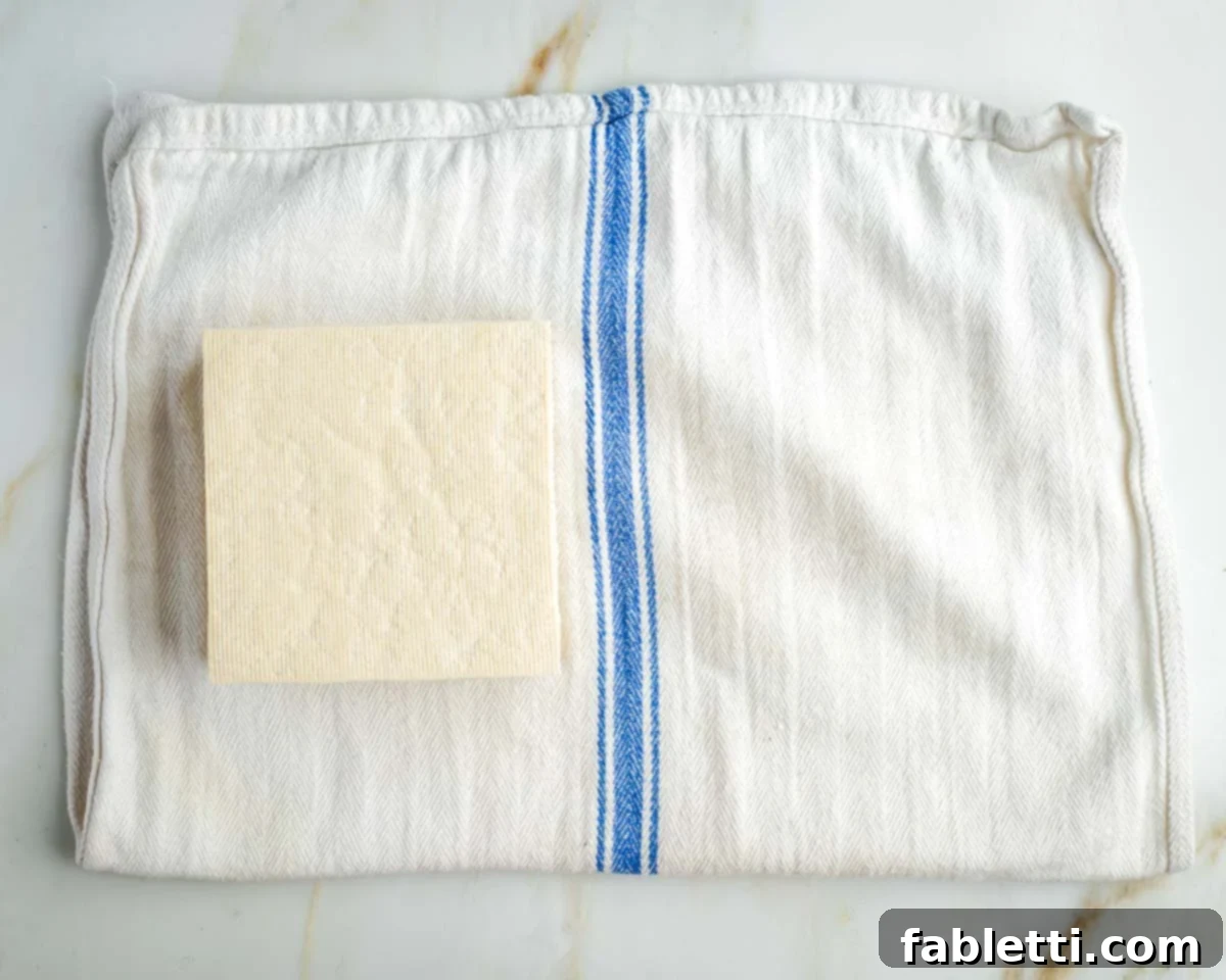 Zingy Vegan Tofu Egg Salad 7 Block of tofu on a white kitchen towel with blue stripe.