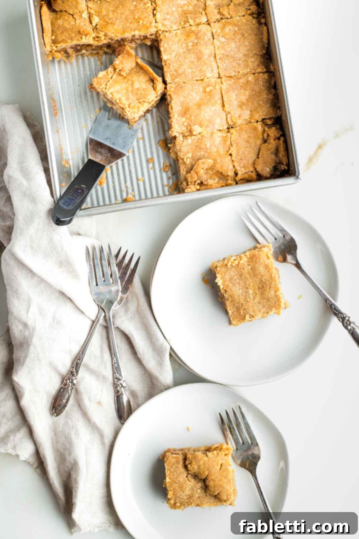 Delicious vegan apple pie bars, golden-brown and ready to be served from a square baking pan, with individual servings on plates beside forks.
