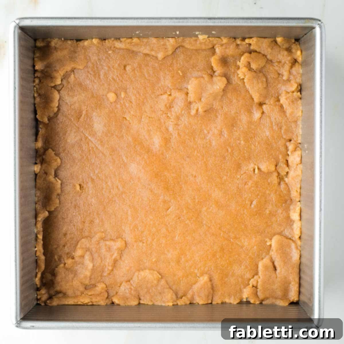 The rolled-out pie dough carefully transferred and pressed into the bottom of an 8x8 inch square baking pan, covering all corners.