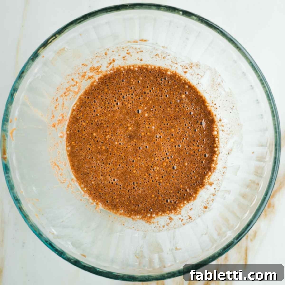 Brown spices combined with maple syrup and lemon juice to create a rich, dark yellow liquid mixture in a bowl.