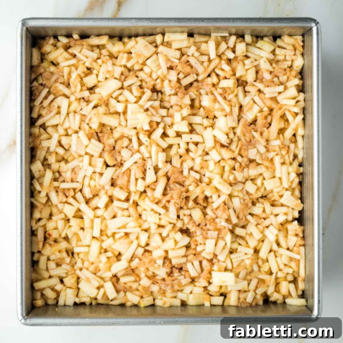 Small pieces of spiced apples spread evenly over the bottom layer of pie dough in a square baking pan.