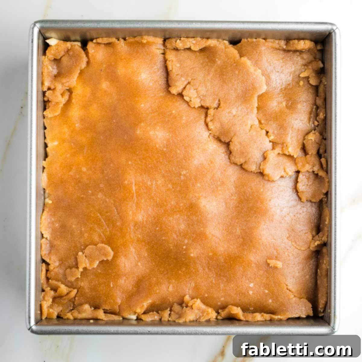 The second piece of pie dough carefully transferred and pieced together to cover the apple filling in the square pan, forming the top crust.