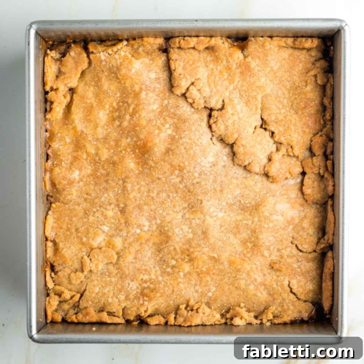 The baked apple pie bars in a square pan, with a golden-brown top crust, fresh out of the oven.