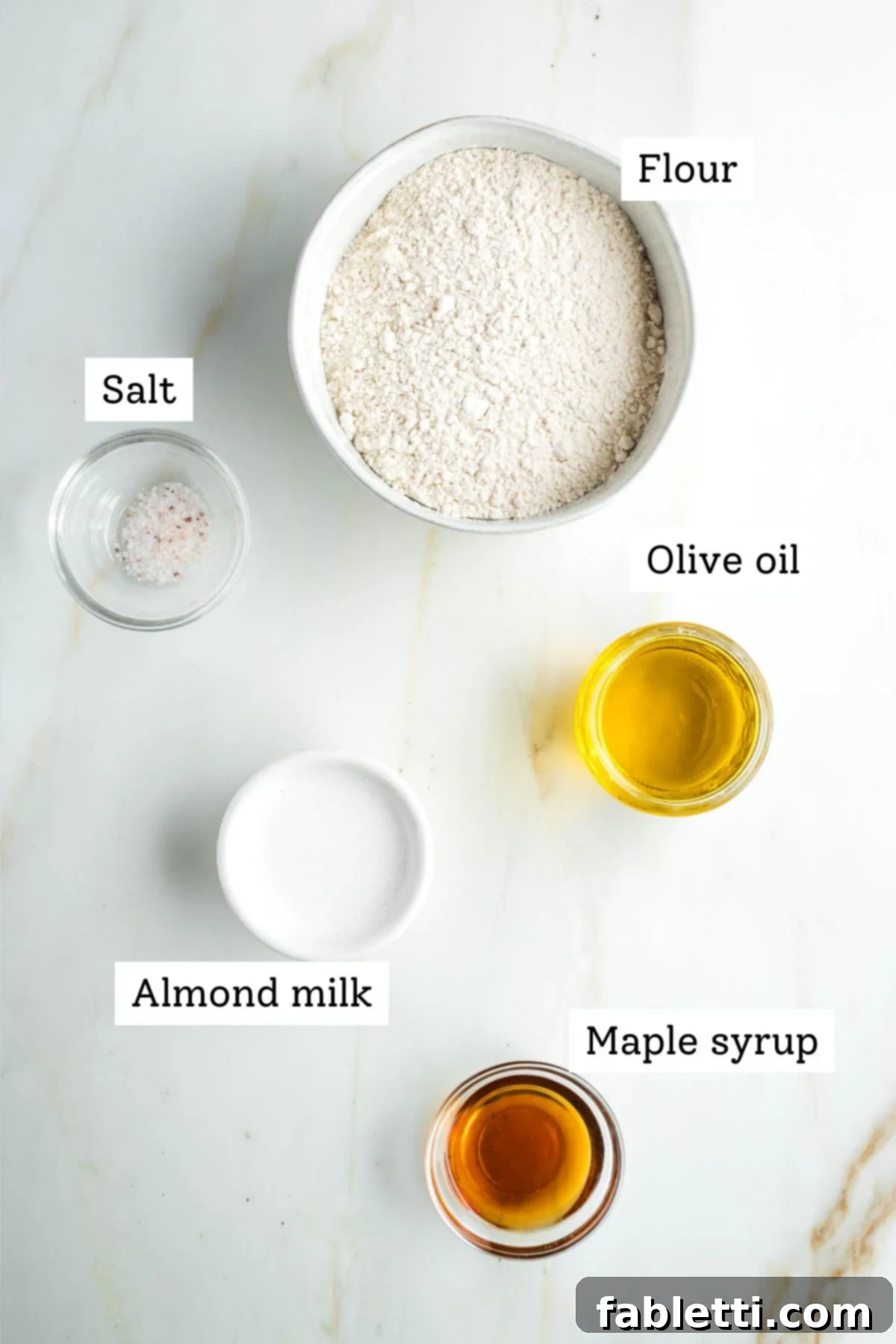 Labeled ingredients for vegan pie crust: flour, salt, olive oil, almond milk, and maple syrup, neatly arranged for preparation.