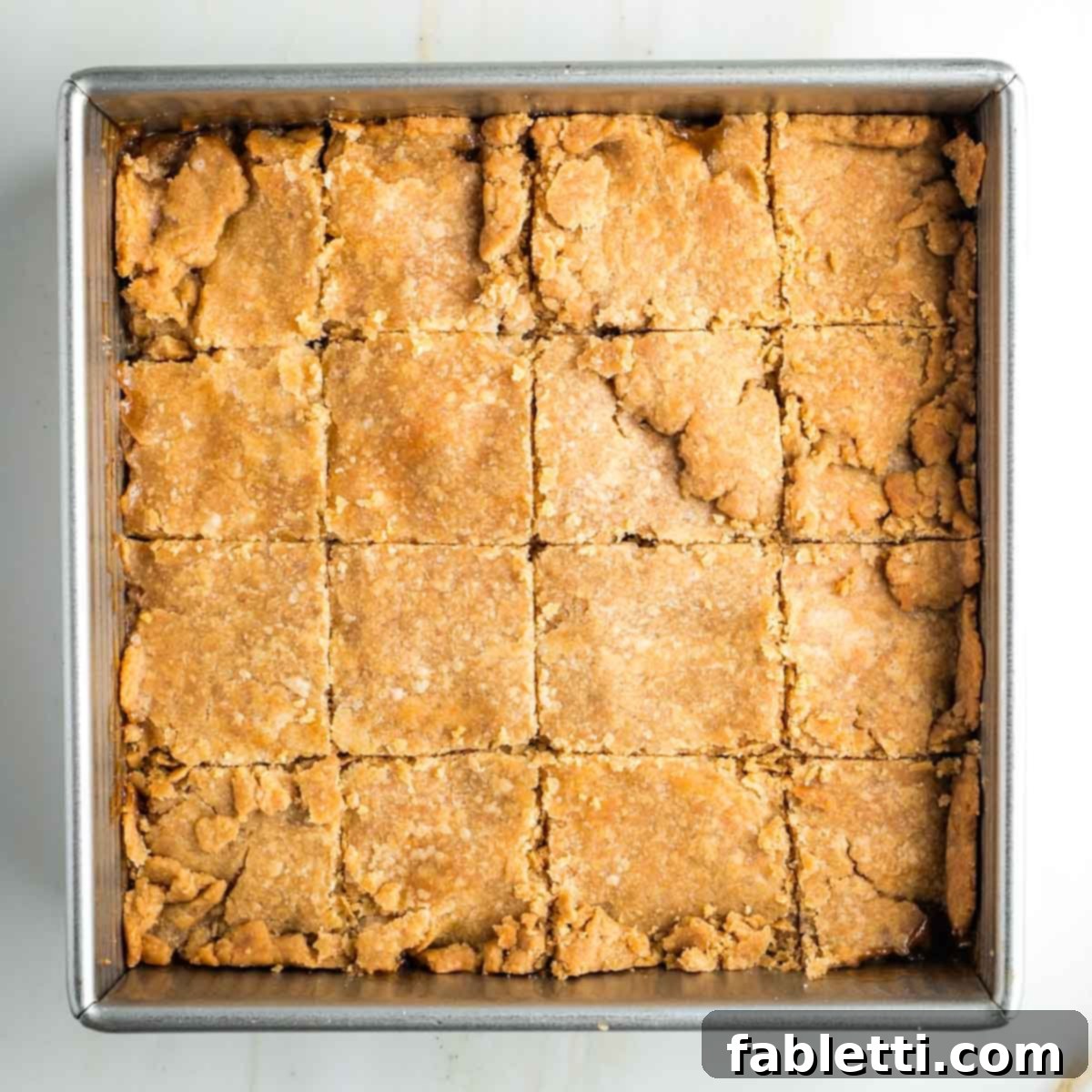The square pan of baked apple pie bars, cooled and cut into uniform squares, ready for serving.