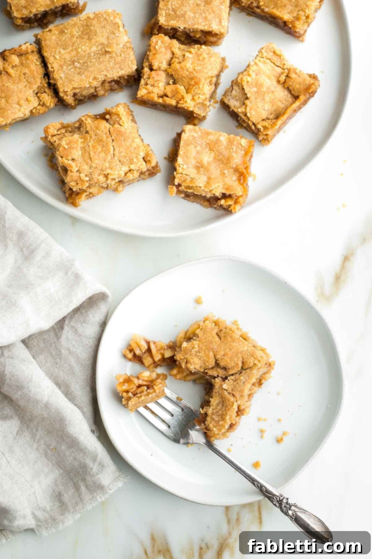 A close-up of baked apple pie bars, with one bar on a plate being eaten with a fork, revealing the luscious apple filling.