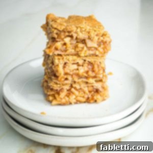 Stack of three apple pie bars with tiny pieces of apples in a thick jammy sauce, nestled between layers of flakey vegan crust.