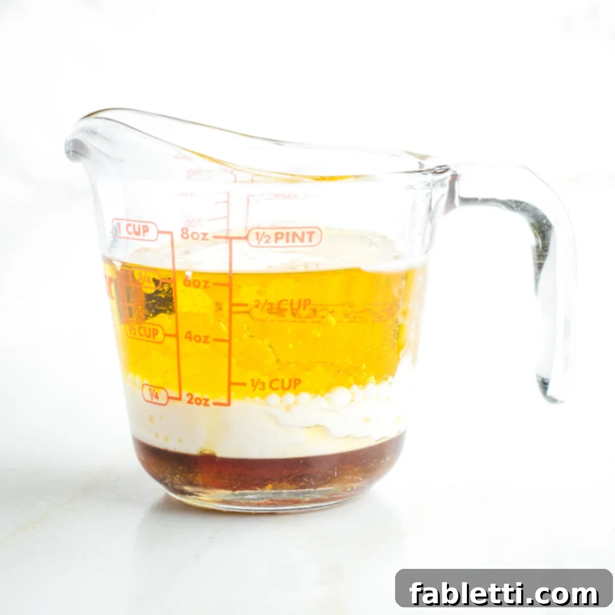 A Pyrex measuring cup filled with a golden liquid mixture of olive oil, almond milk, and maple syrup.
