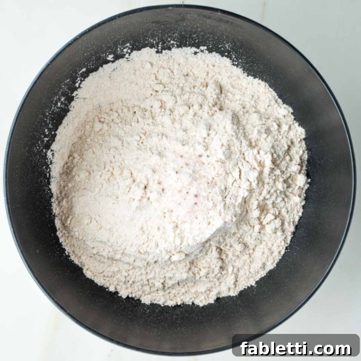 Flour and salt are combined in a black mixing bowl, ready for aeration.