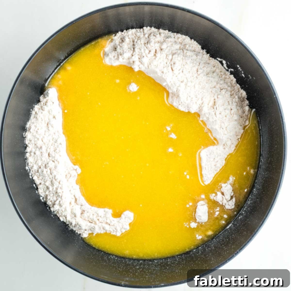 Yellow liquid mixture being poured onto the dry flour and salt in a black mixing bowl.