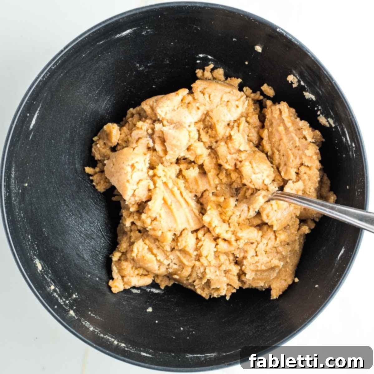 Lumpy pie dough forming in a black bowl, showing the consistency before it's fully cohesive.
