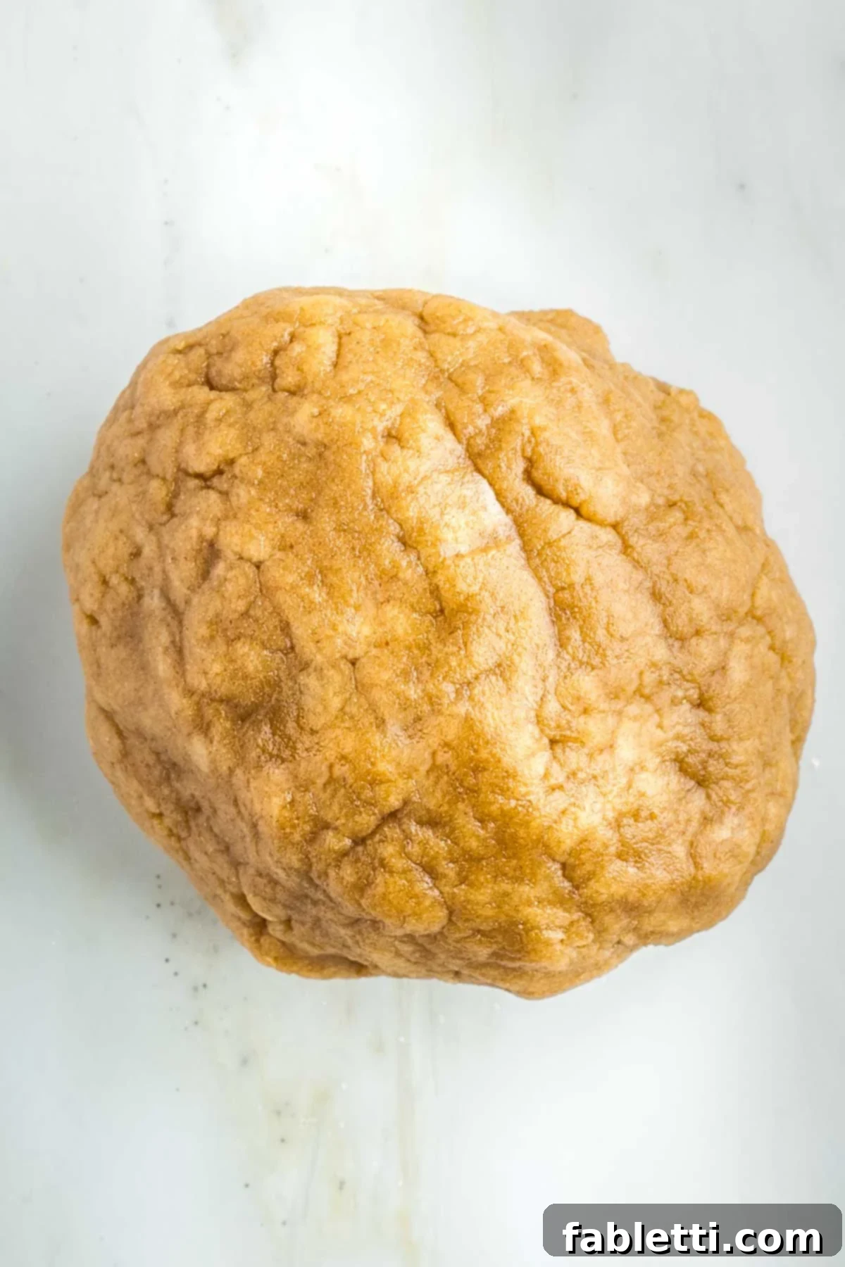 A large, somewhat lumpy ball of pie dough on a clean counter, divided into two pieces.