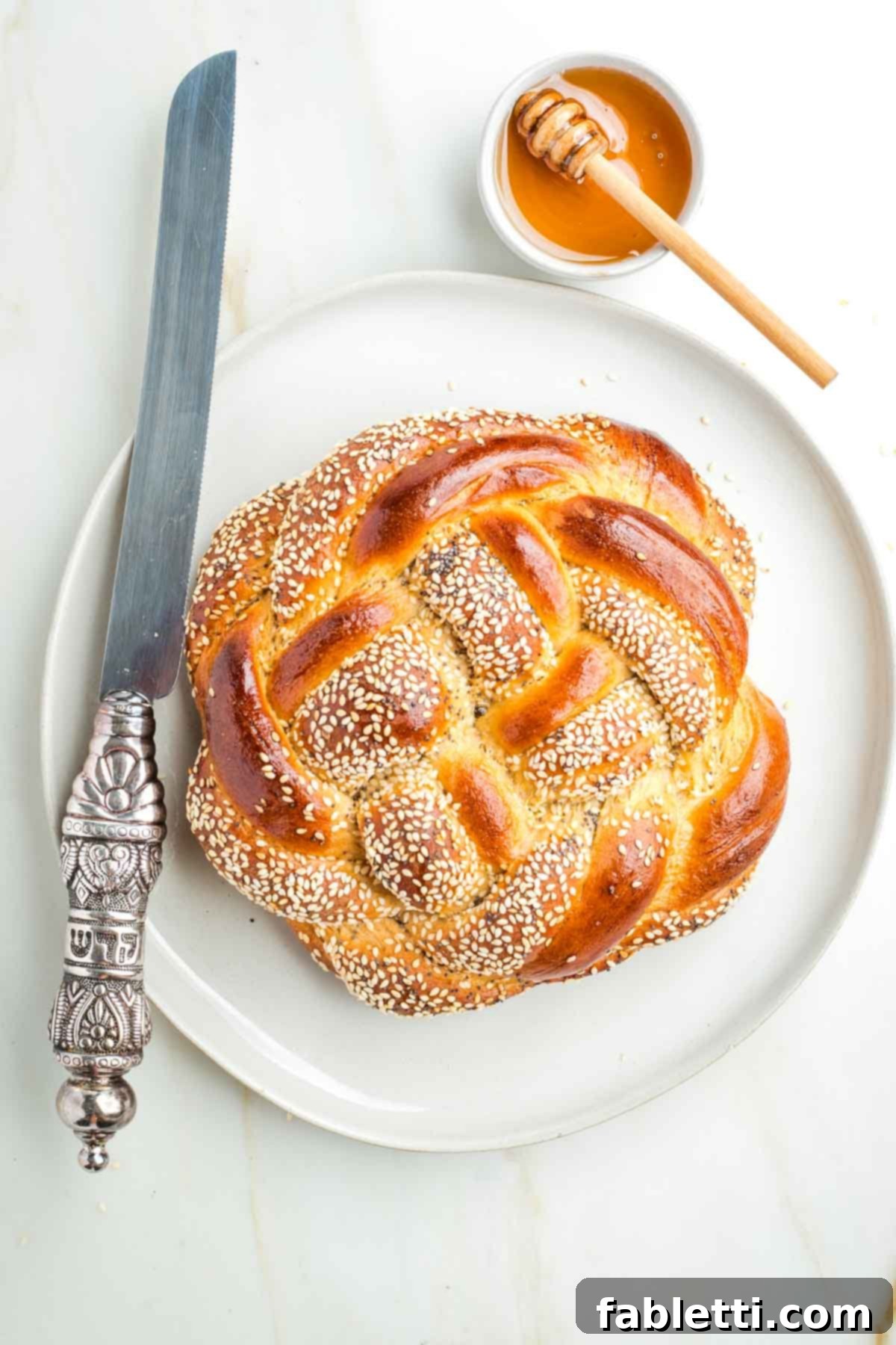 Pillowy Sweet Challah Crown 2 Round, braided challah loaves, generously sprinkled with sesame and poppy seeds, displayed alongside a dish of glistening honey and a serrated challah knife, ready for a festive meal.