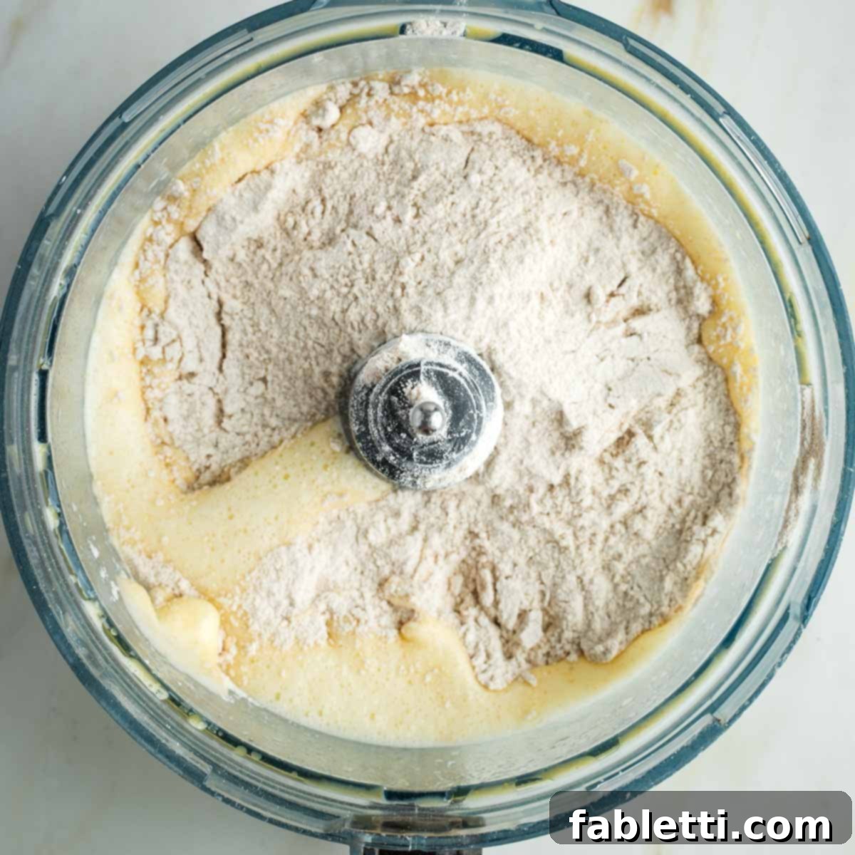 Pillowy Sweet Challah Crown 11 Half of the measured flour has been sprinkled evenly on top of the active yeast and egg mixture within the food processor bowl.