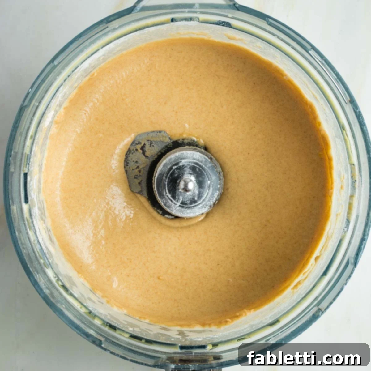 Pillowy Sweet Challah Crown 12 A creamy, tan-colored mixture forming in the food processor, halfway to becoming a cohesive bread dough.