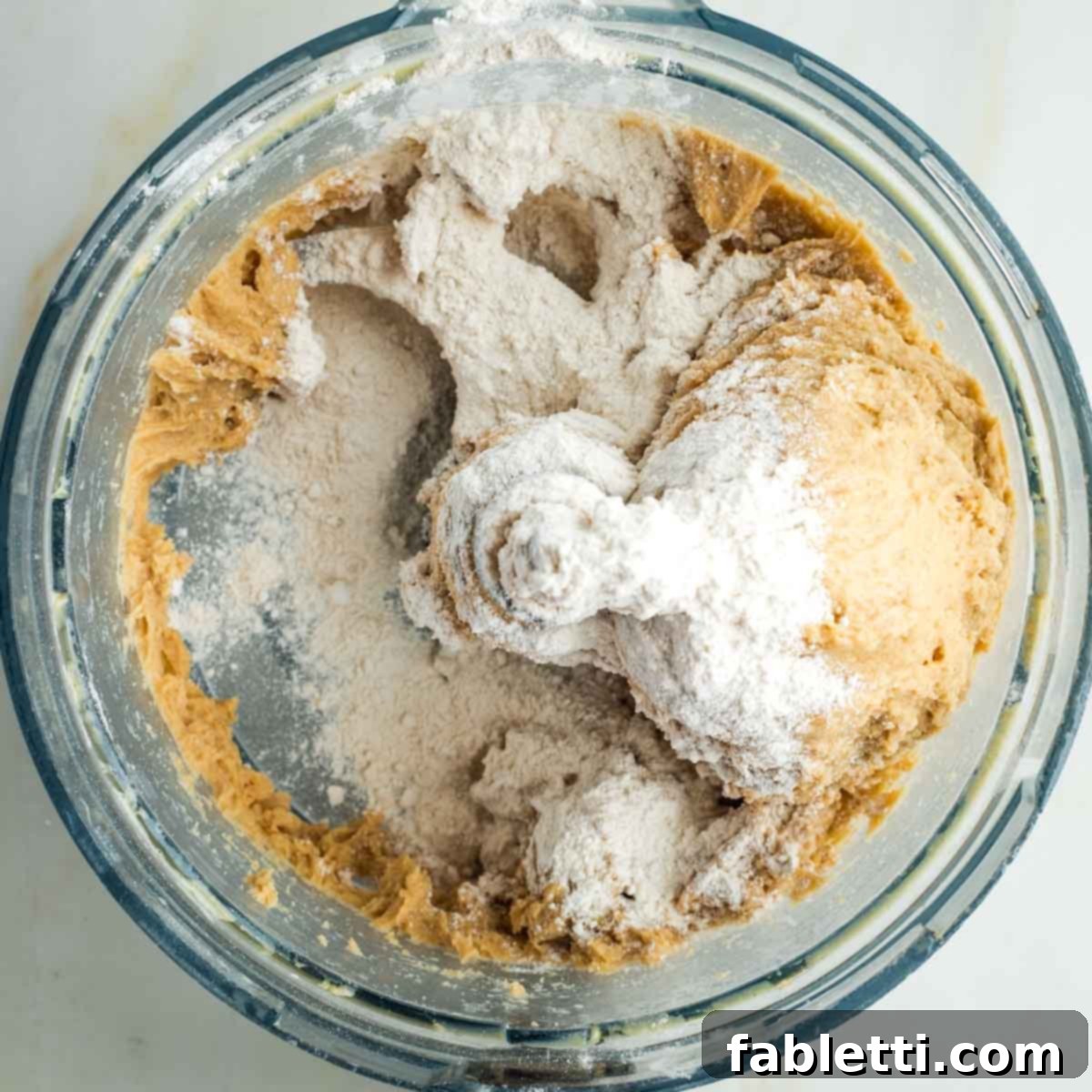 Pillowy Sweet Challah Crown 15 A small amount of flour, precisely one tablespoon, is sprinkled onto the sticky bread dough in the food processor bowl to adjust consistency.