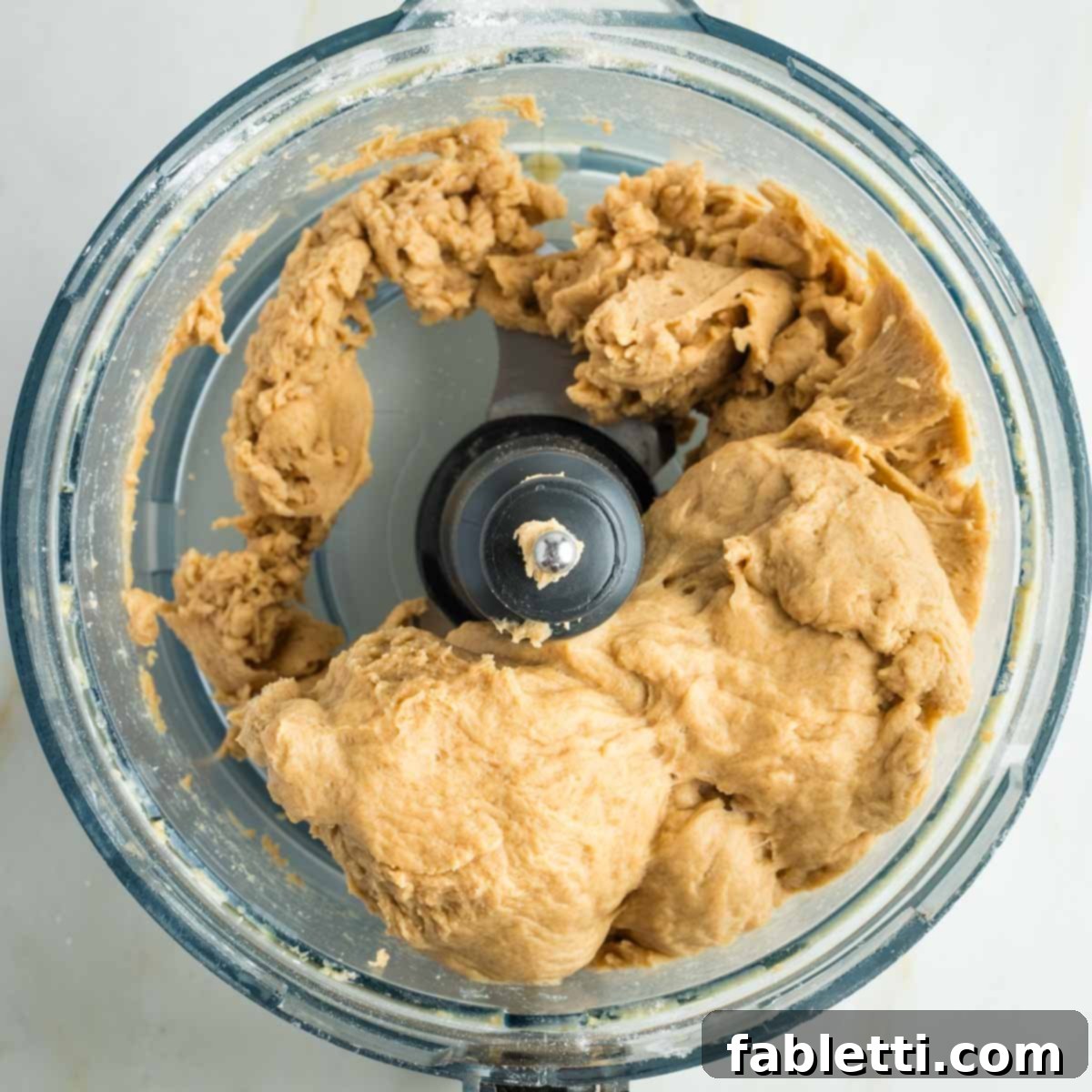 Pillowy Sweet Challah Crown 16 Perfectly kneaded bread dough gracefully pulling away from the sides of a food processor bowl, indicating ideal consistency.