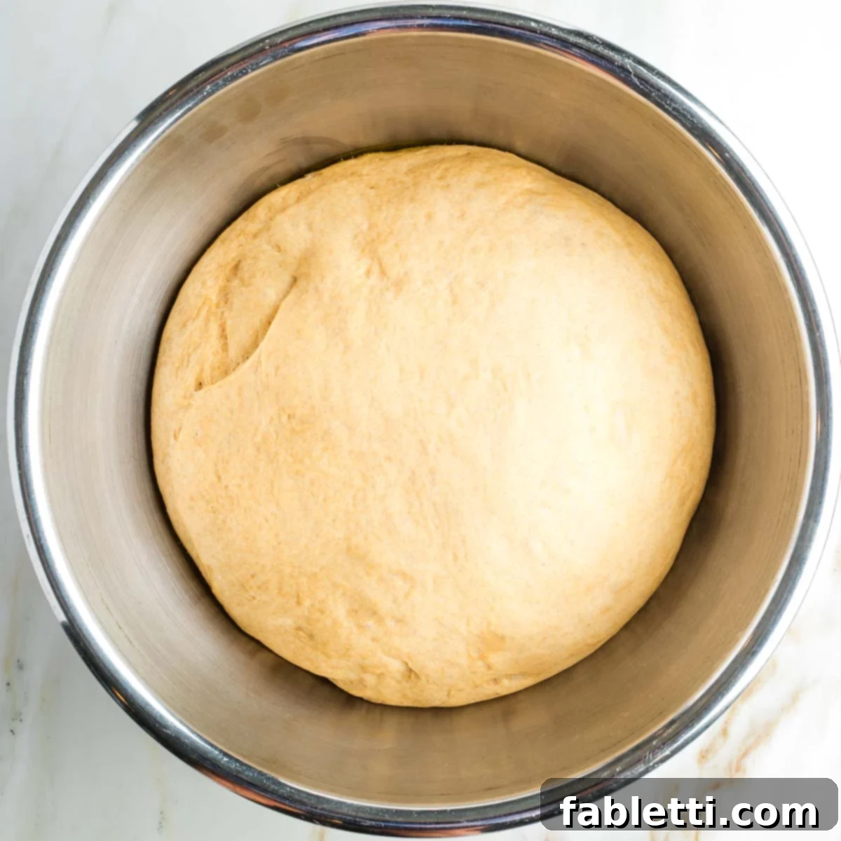 Pillowy Sweet Challah Crown 20 A large metal bowl holds a significantly risen and airy ball of challah dough, expanded to more than double its original size after its first proof.