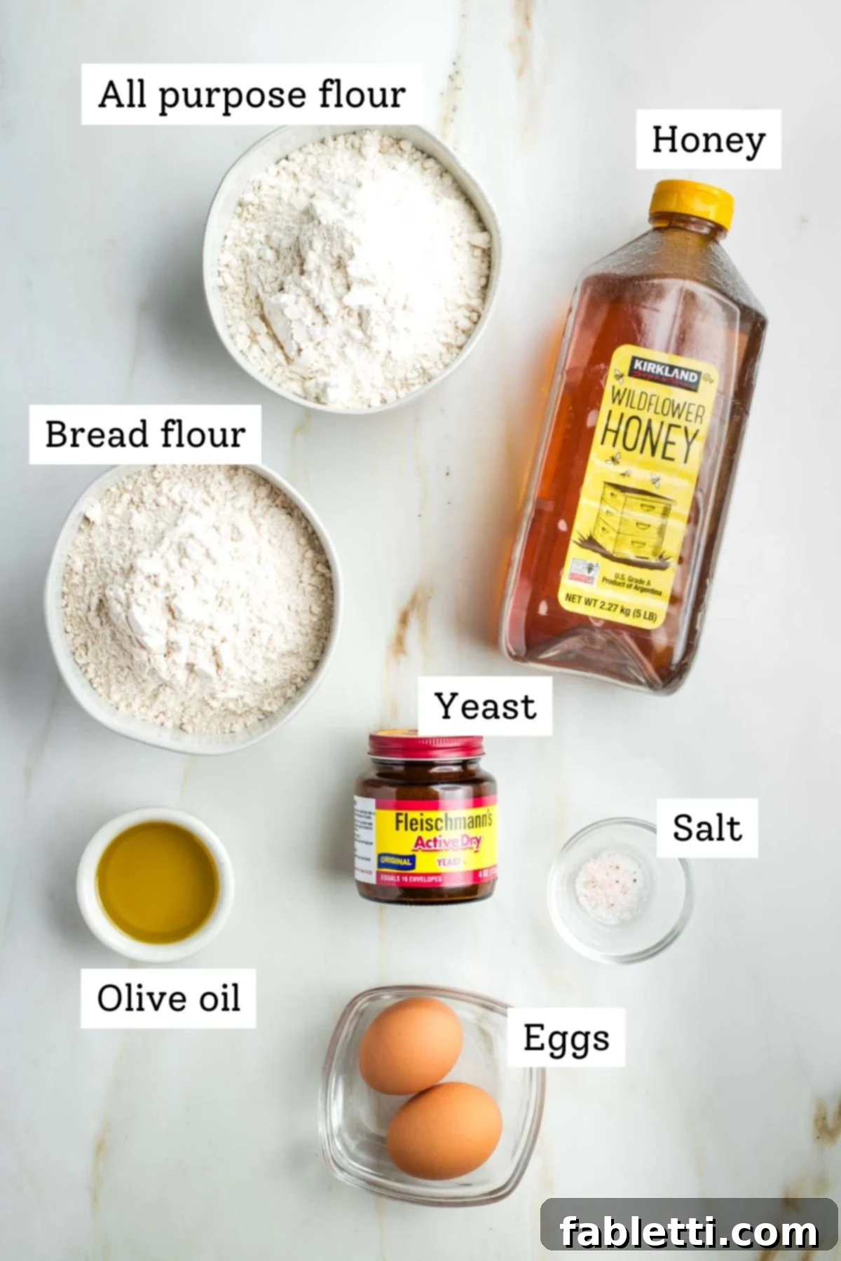 Pillowy Sweet Challah Crown 3 Clearly labeled ingredients for homemade challah bread: flour, honey, yeast, olive oil, salt, and eggs, neatly arranged for baking.