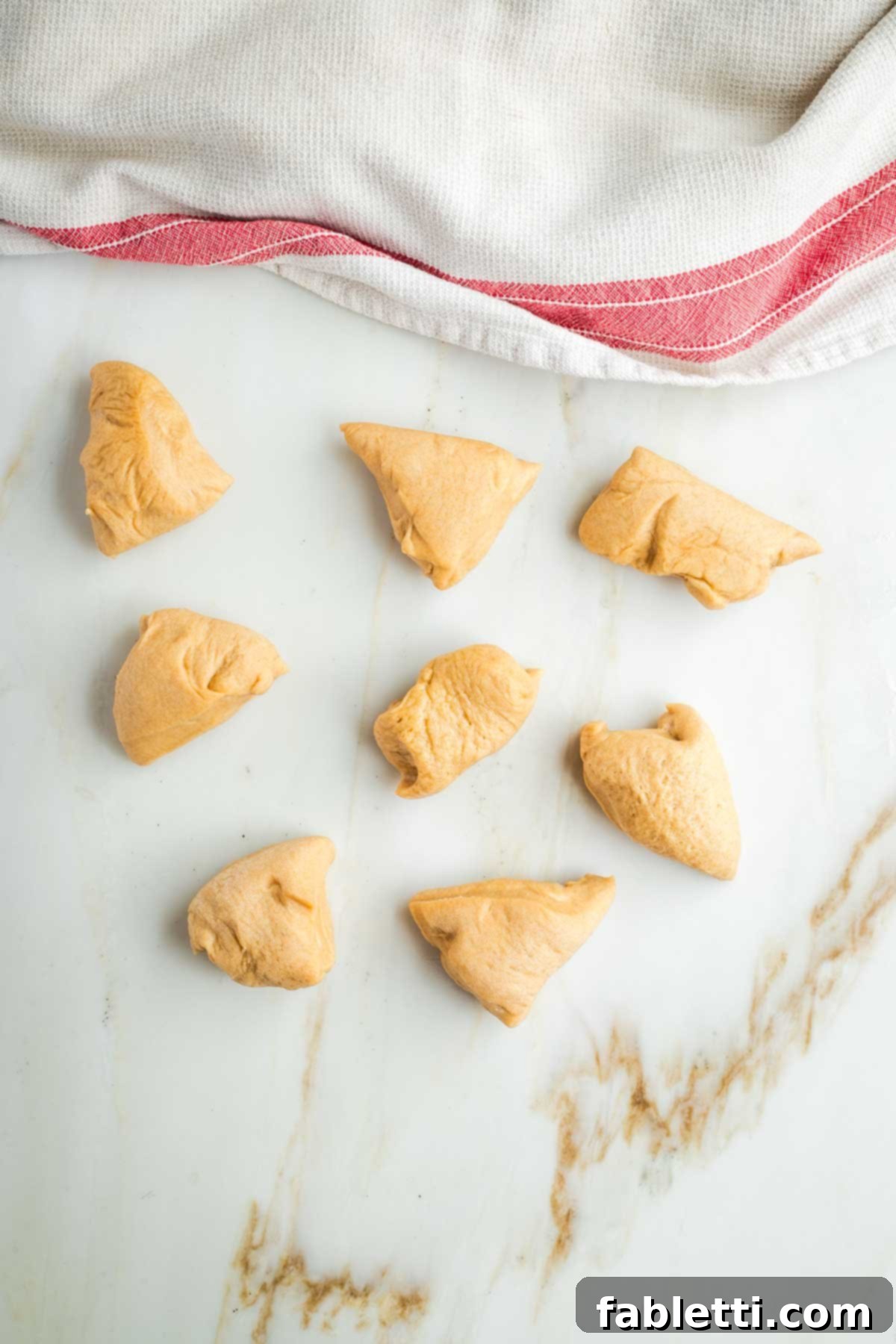 Pillowy Sweet Challah Crown 22 Eight small pieces of challah dough are visible, while a kitchen towel thoughtfully covers the remaining dough pieces to prevent them from drying out during the braiding process.