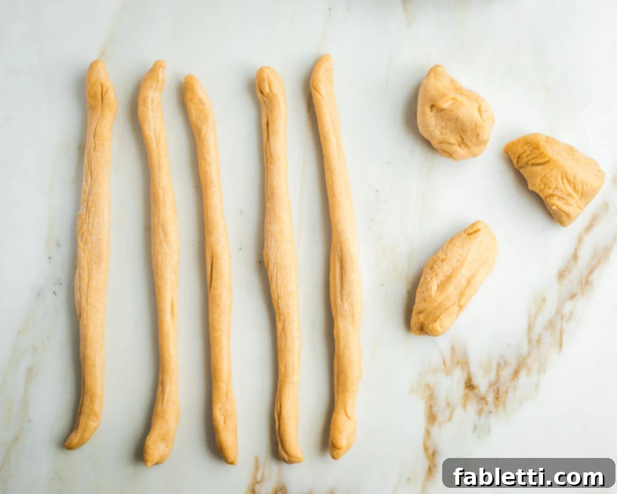 Pillowy Sweet Challah Crown 23 Three initial pieces of challah dough alongside five rolled-out, rope-like strands of dough, demonstrating the transformation from ball to rope.