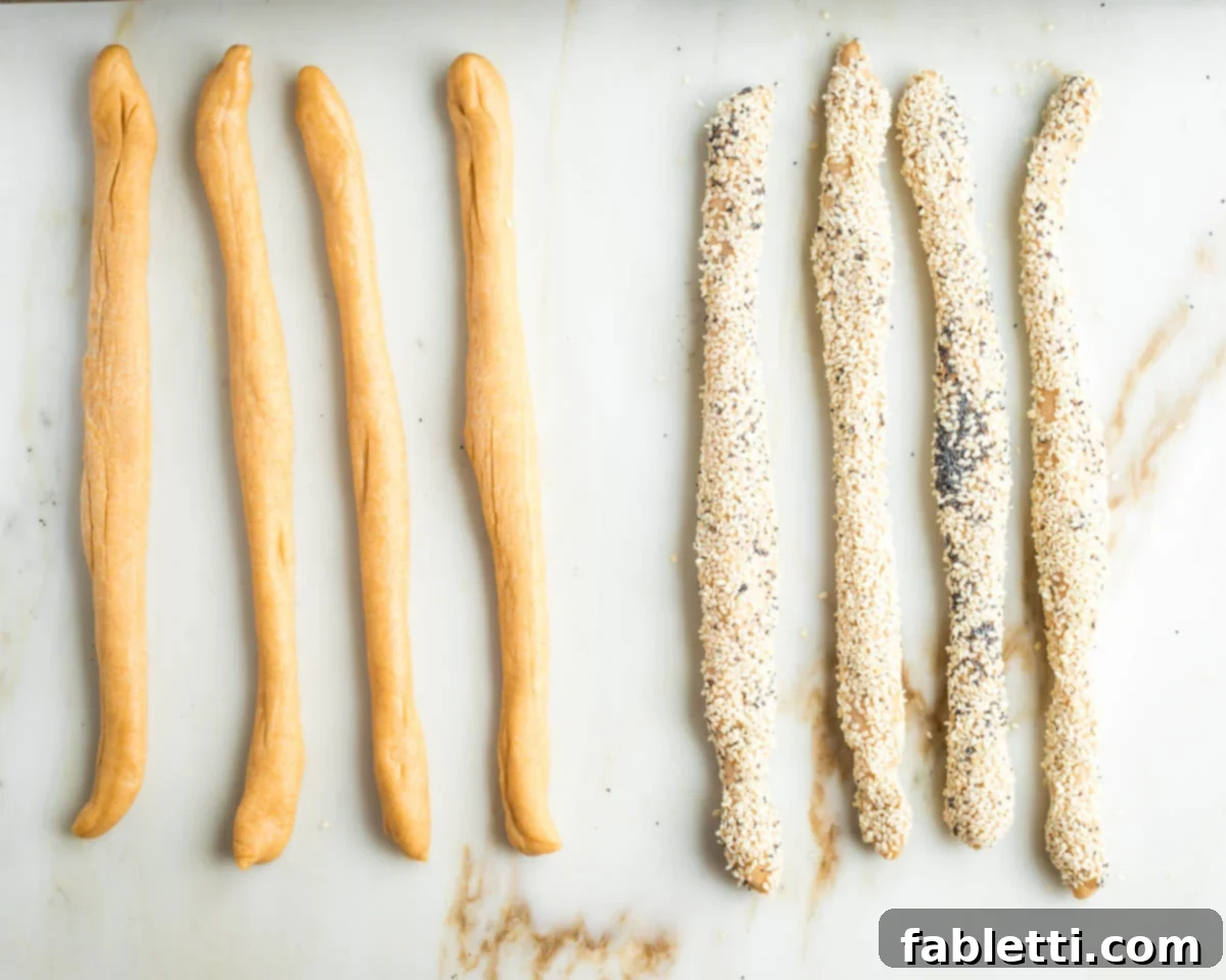 Pillowy Sweet Challah Crown 26 A close-up view showing a challah dough strand being rolled through a mixture of sesame and poppy seeds after being moistened with water, creating an even coating.