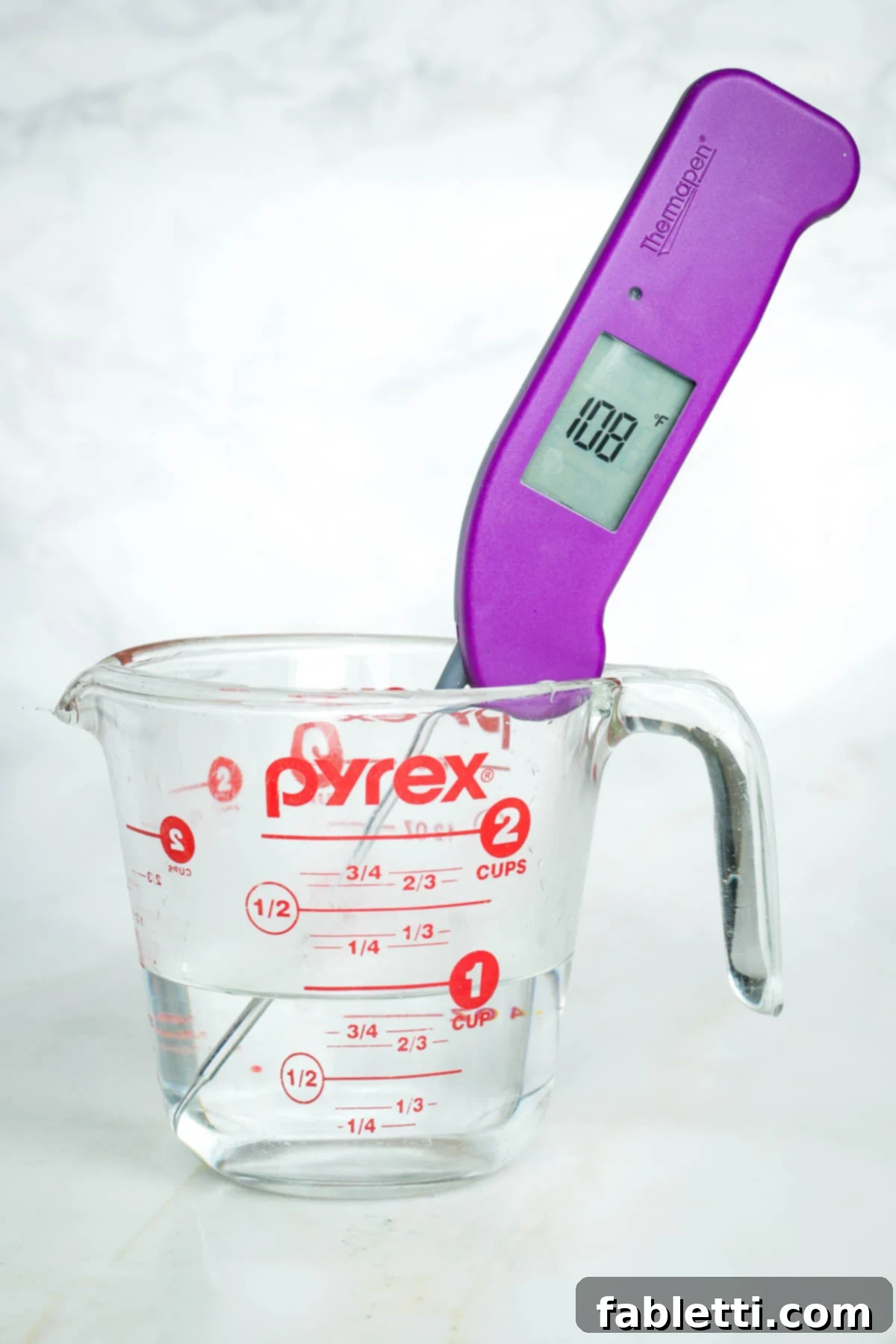 Pillowy Sweet Challah Crown 4 A kitchen thermometer accurately displays 108 degrees Fahrenheit within a clear glass cup of water, indicating the perfect temperature for activating yeast.