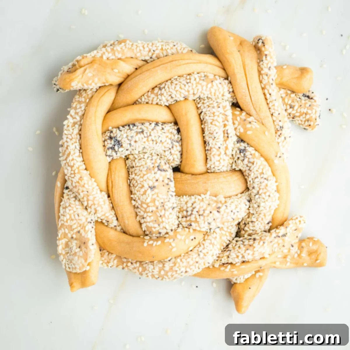 Pillowy Sweet Challah Crown 31 An almost completed 8-strand challah braid, showing seeded and plain dough strands intricately woven in an over-under pattern, with the ends gathered and ready to be tucked.