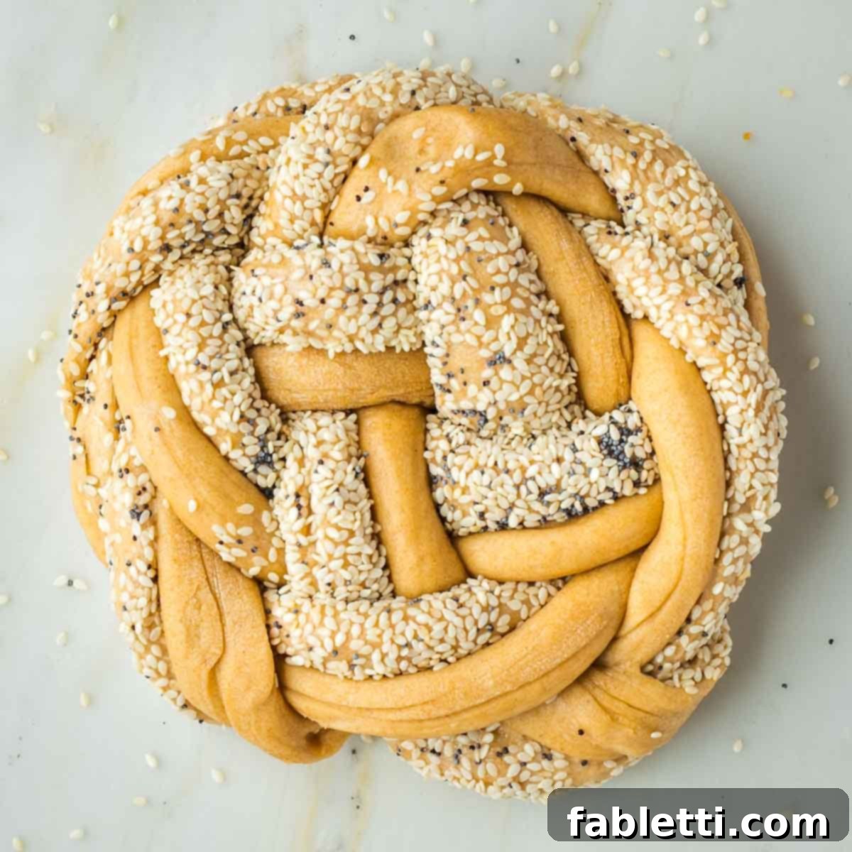Pillowy Sweet Challah Crown 32 A perfectly shaped round loaf of braided challah dough, adorned with sesame and poppy seeds, with all ends neatly tucked underneath for a smooth, finished appearance.