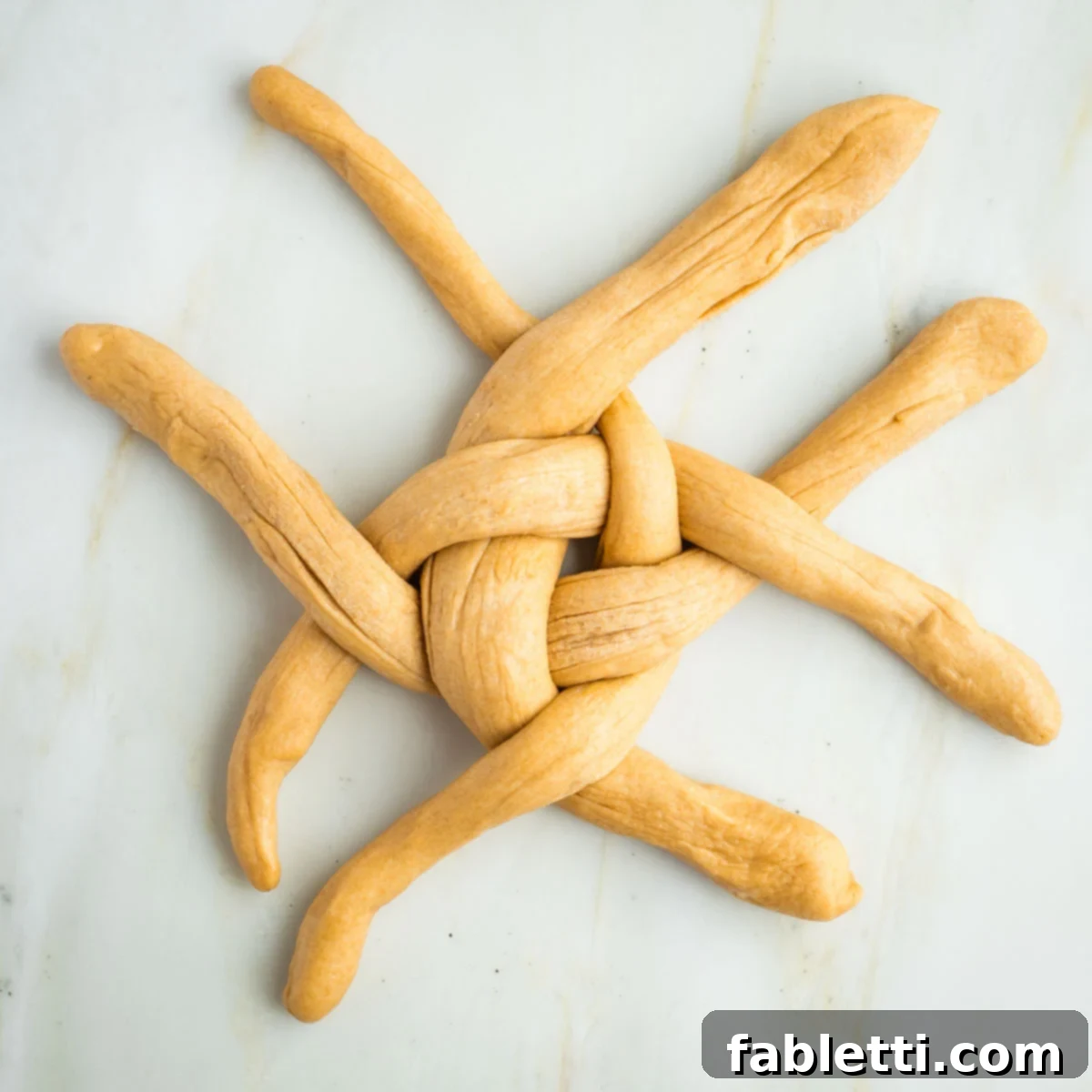 Pillowy Sweet Challah Crown 35 Long ropes of dough alternating over and under in a cross pattern.