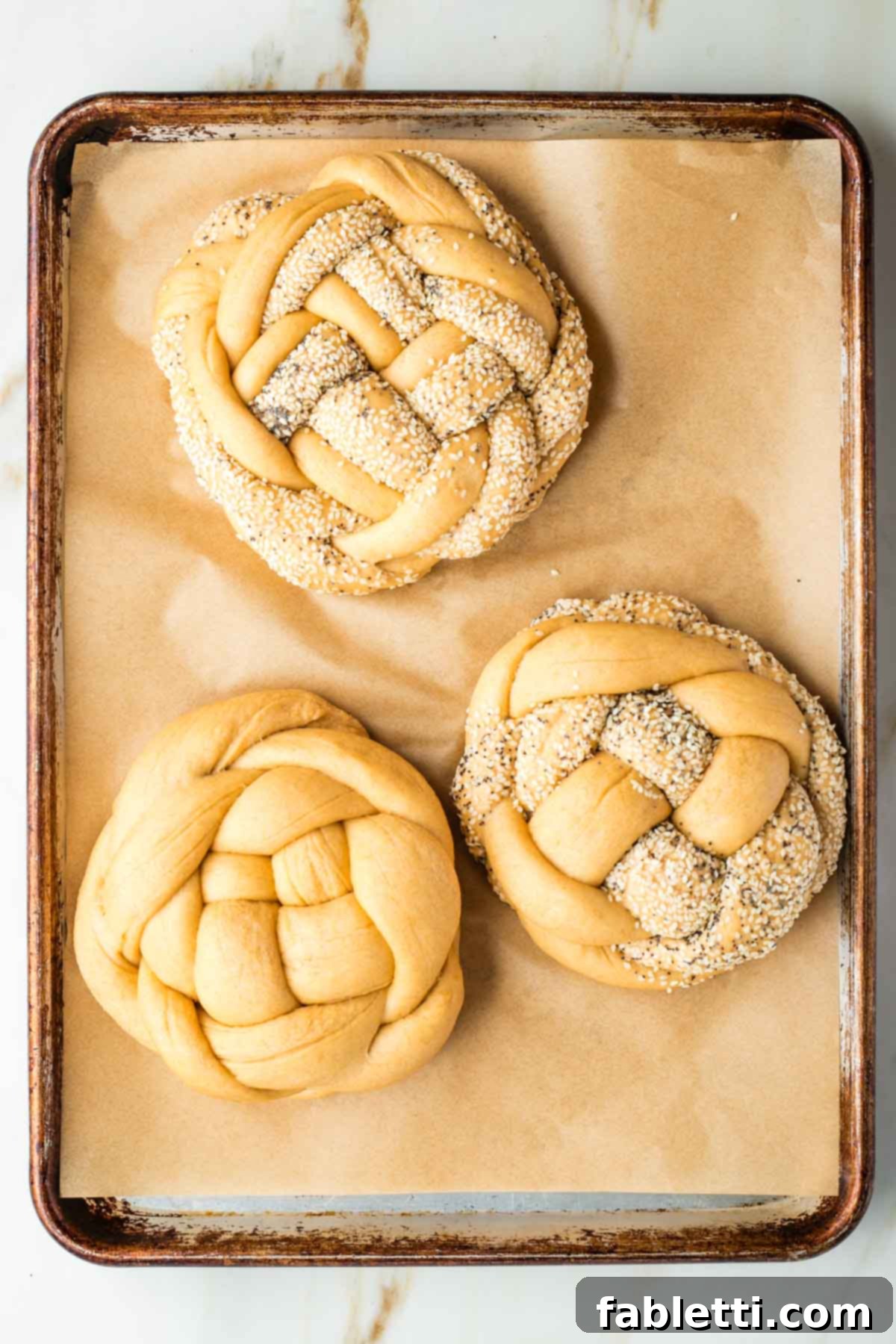 Pillowy Sweet Challah Crown 40 Large, fluffy, and visibly expanded round, braided loaves of unbaked challah bread rest on a parchment-lined rimmed baking tray, having completed their second rise.