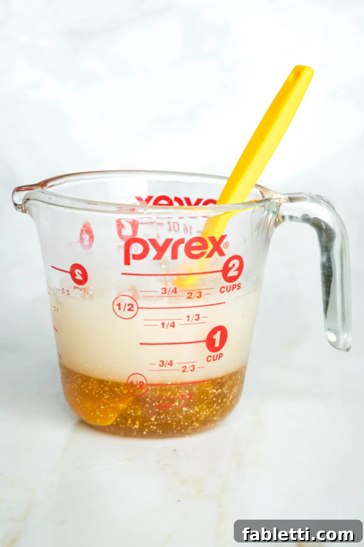 Pillowy Sweet Challah Crown 5 A side view of a glass measuring cup with water, honey, and yeast actively proofing, showing initial bubbling.