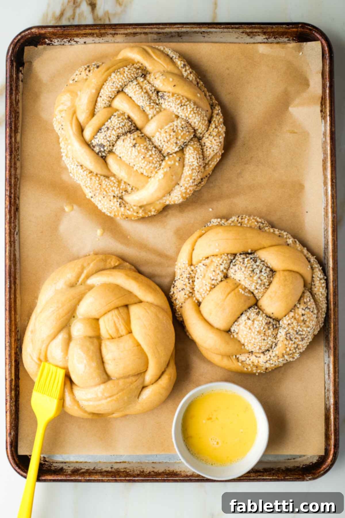 Pillowy Sweet Challah Crown 41 Brushing egg wash on braided round loaves of challah bread.