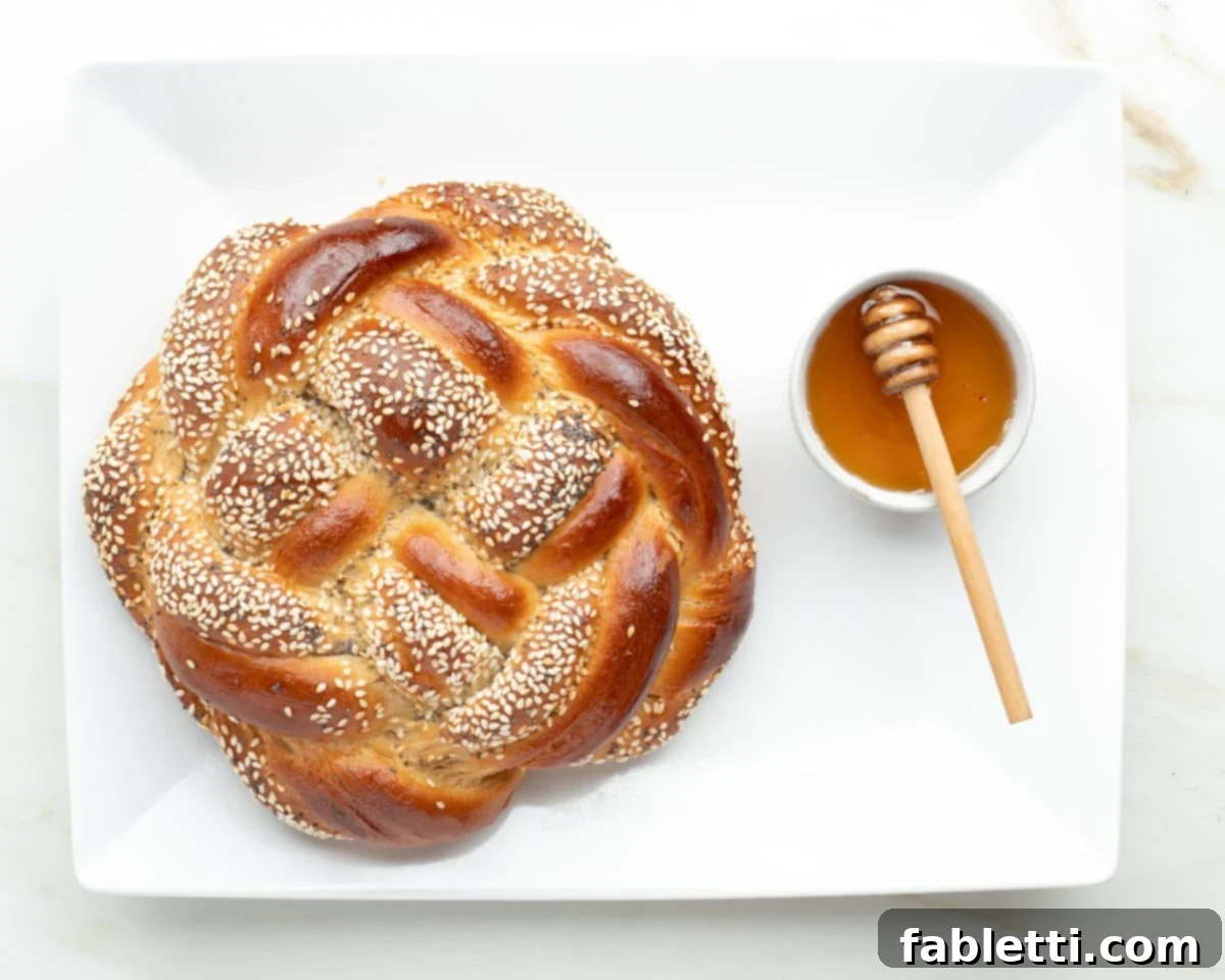 Pillowy Sweet Challah Crown 45 A beautifully baked round, braided challah bread, adorned with sesame seeds, presented alongside a small, inviting dish of honey, embodying a sweet holiday tradition.
