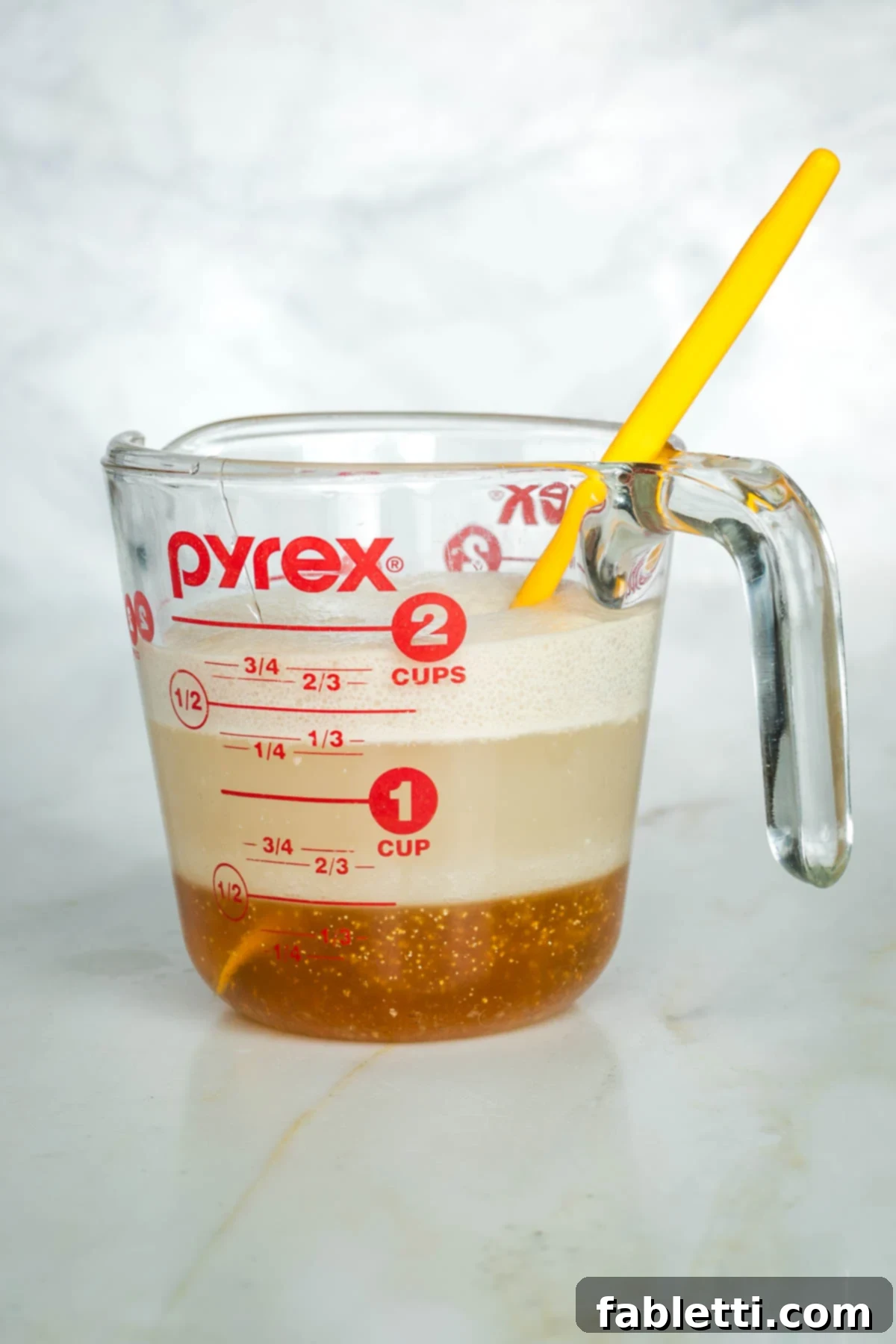 Pillowy Sweet Challah Crown 6 A side view of the yeast, honey, and water mixture vigorously bubbling and expanding, showing successful proofing in a glass measuring cup.