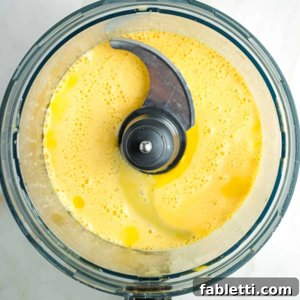Pillowy Sweet Challah Crown 9 The food processor bowl contains a frothy, emulsified mixture of whipped eggs and olive oil, indicating proper blending.