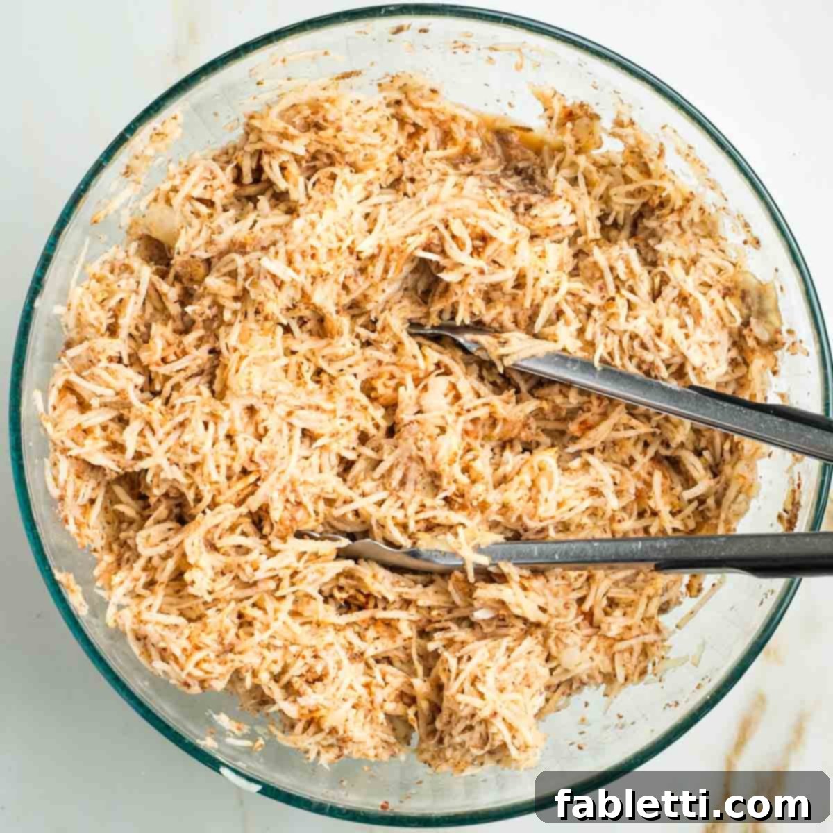 Ultimate Vegan Potato Kugel 11 Large set of tongs, tossing together shredded potatoes with spices.