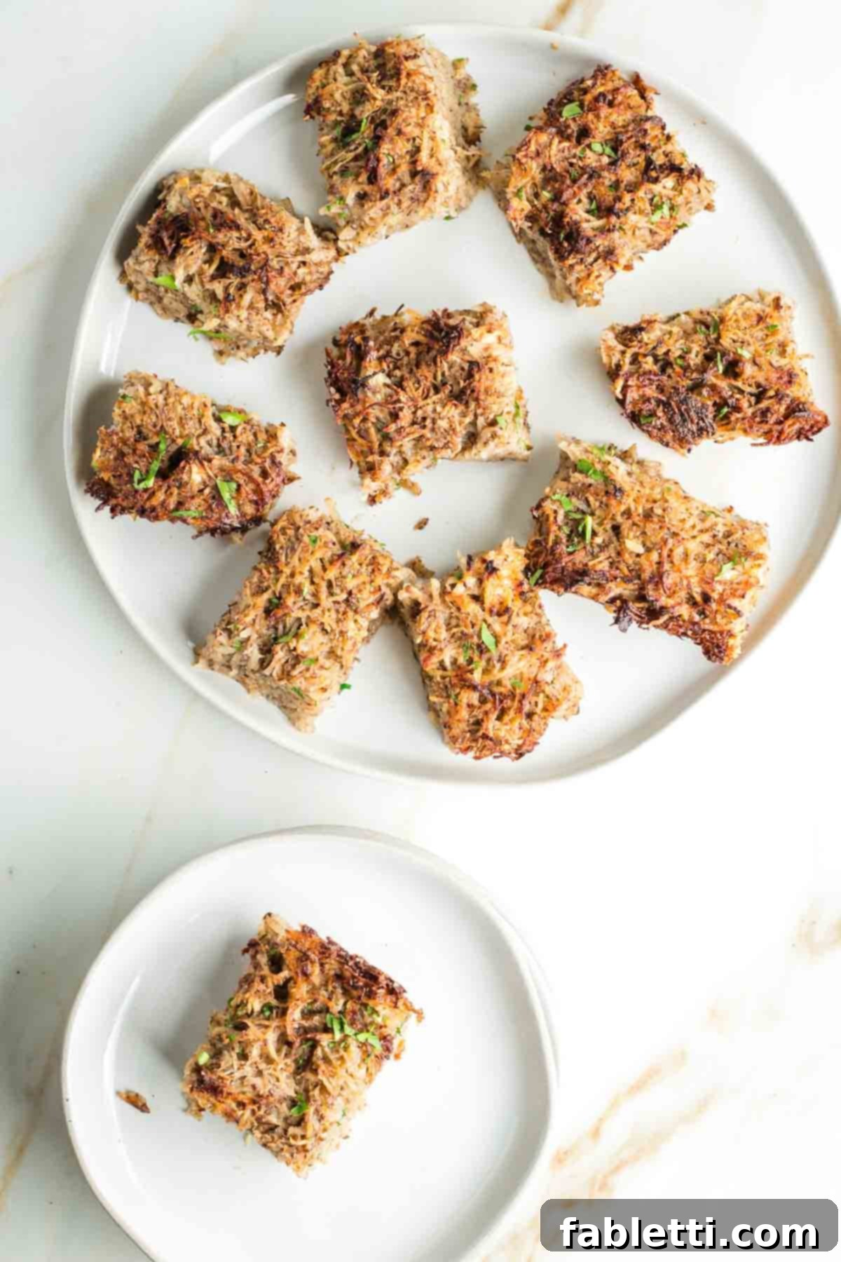 Ultimate Vegan Potato Kugel 16 Squares of golden-brown potato kugel on a plate, with an additional piece on a smaller plate, ready to be enjoyed.