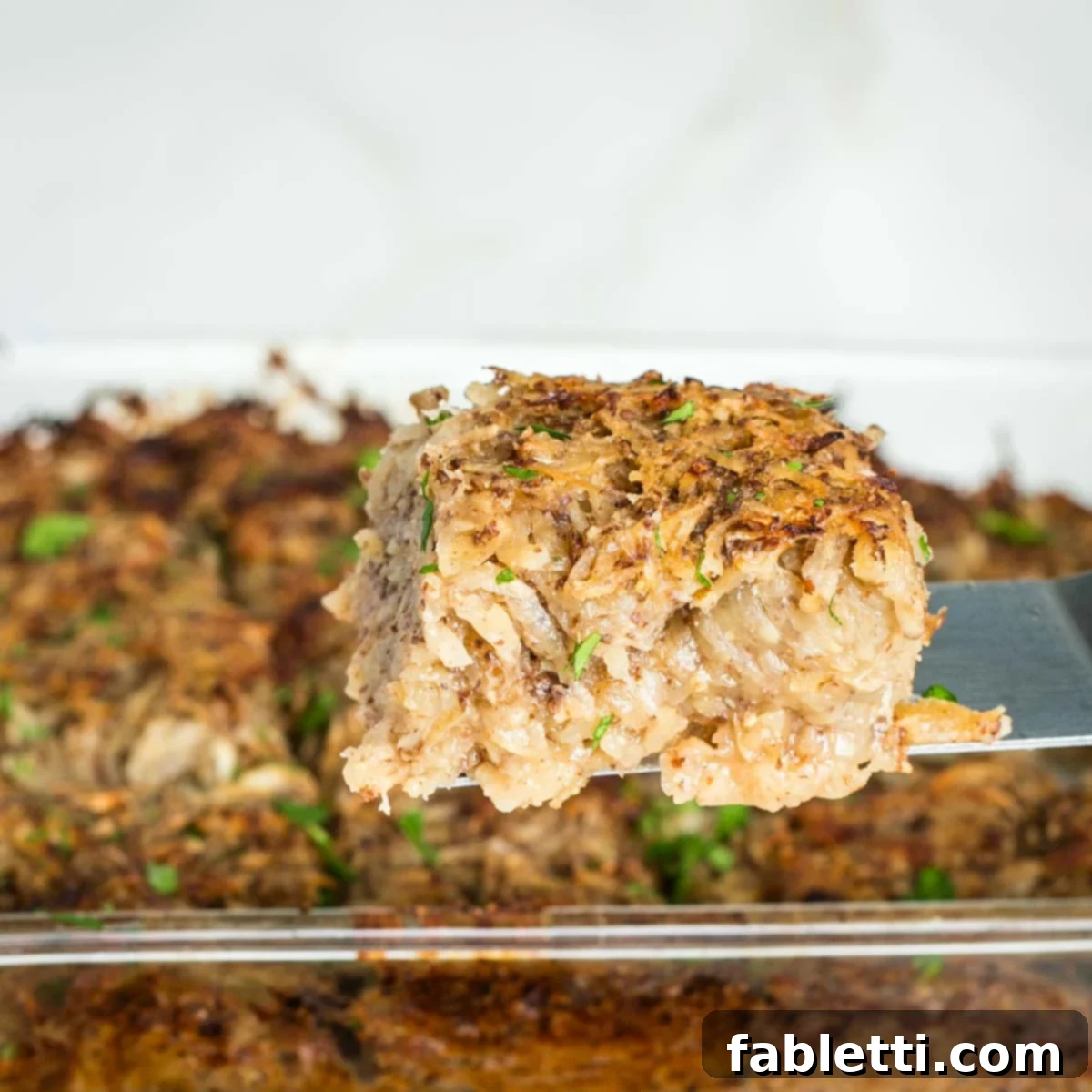 Ultimate Vegan Potato Kugel 18 Side view of a piece of vegan potato kugel being lifted from the baking pan with a spatula, showcasing its appealing crispy bottom.