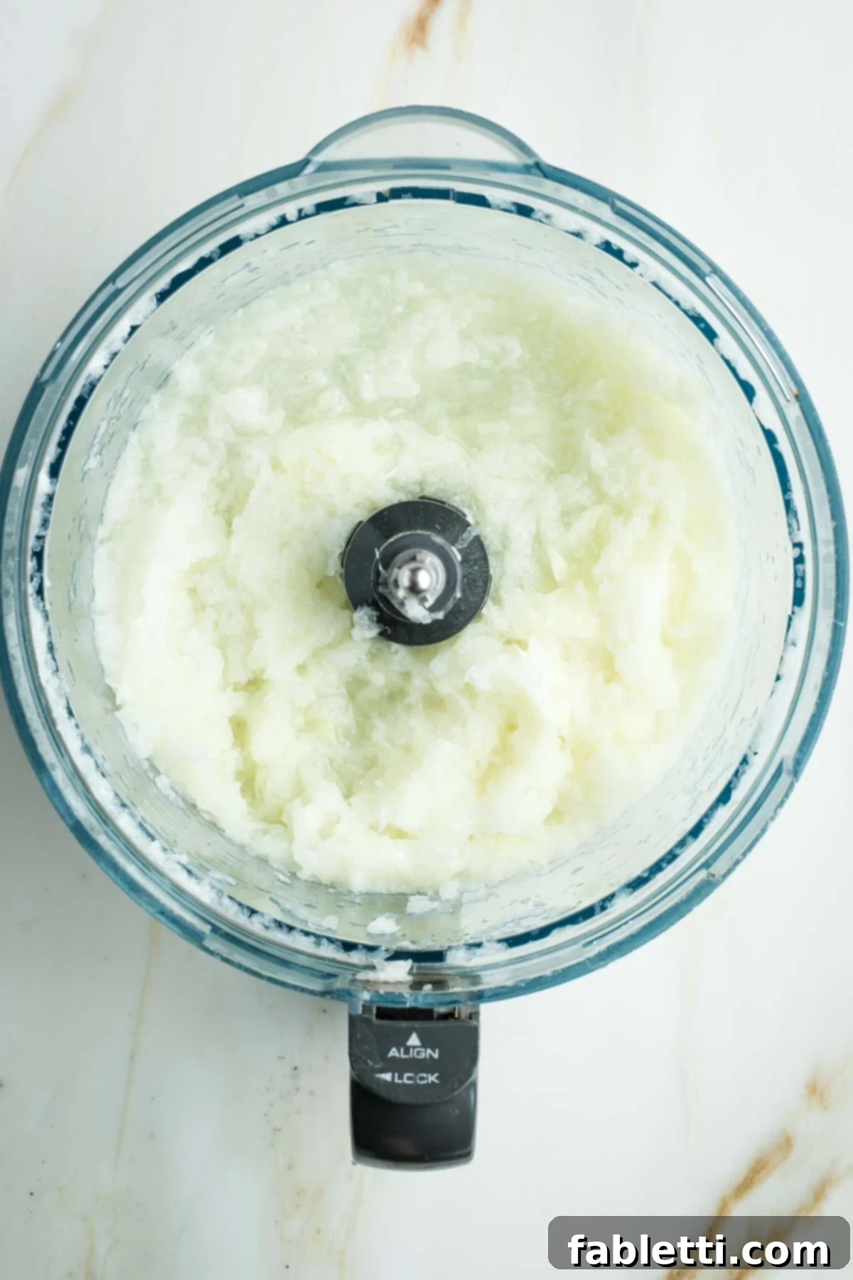 Ultimate Vegan Potato Kugel 5 Shredded onions, watery in the bowl of a food processor.