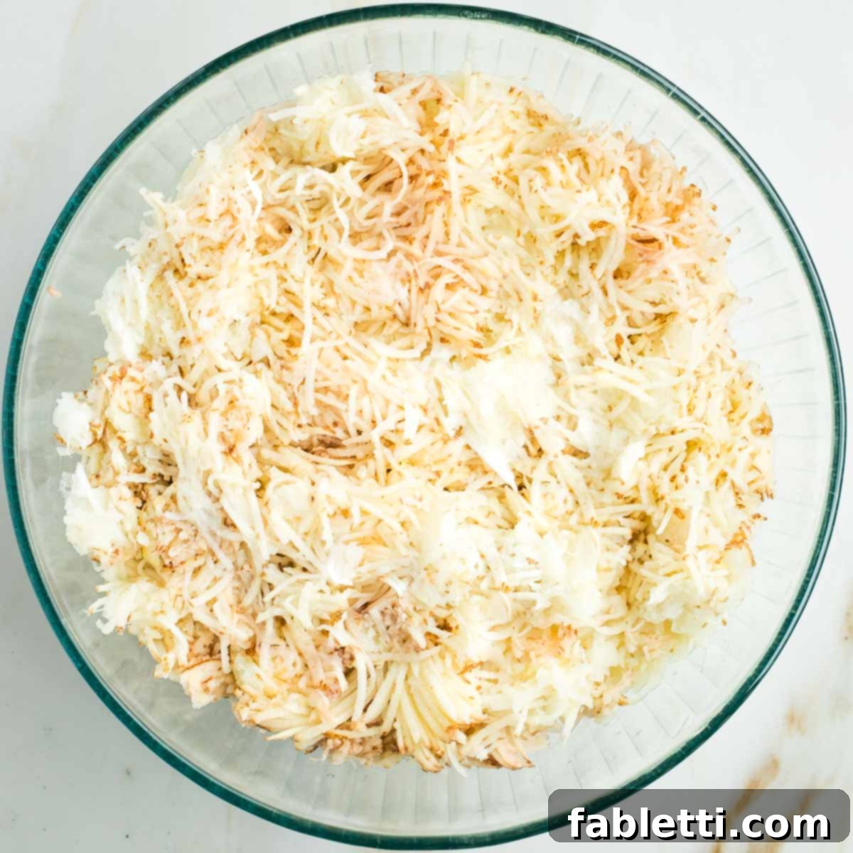 Ultimate Vegan Potato Kugel 9 Thinly shredded unpeeled potatoes and onions in a large glass bowl.